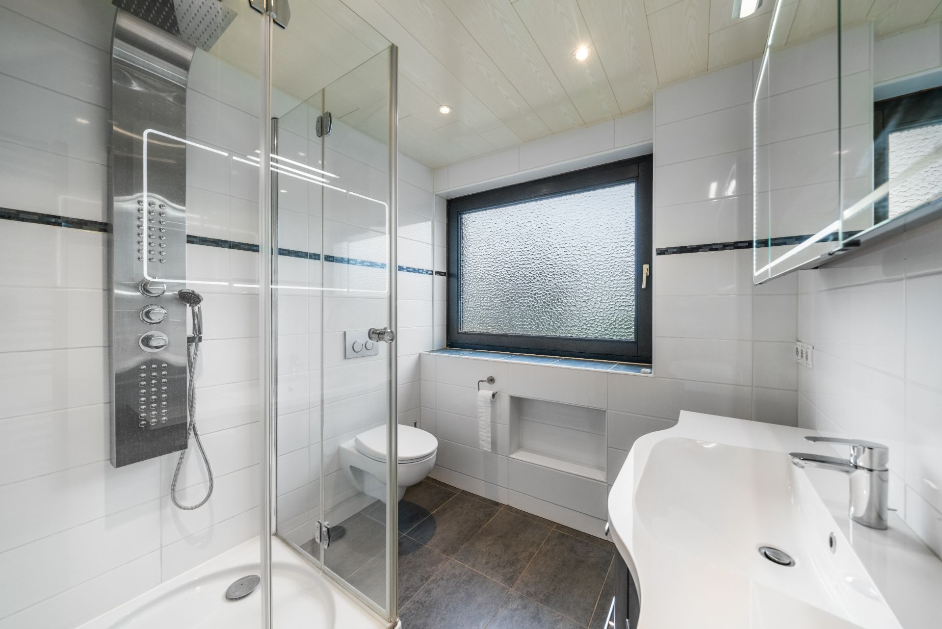 Modernes Bad mit Dusche, WC, Waschbecken und großem Fenster mit Milchglas.