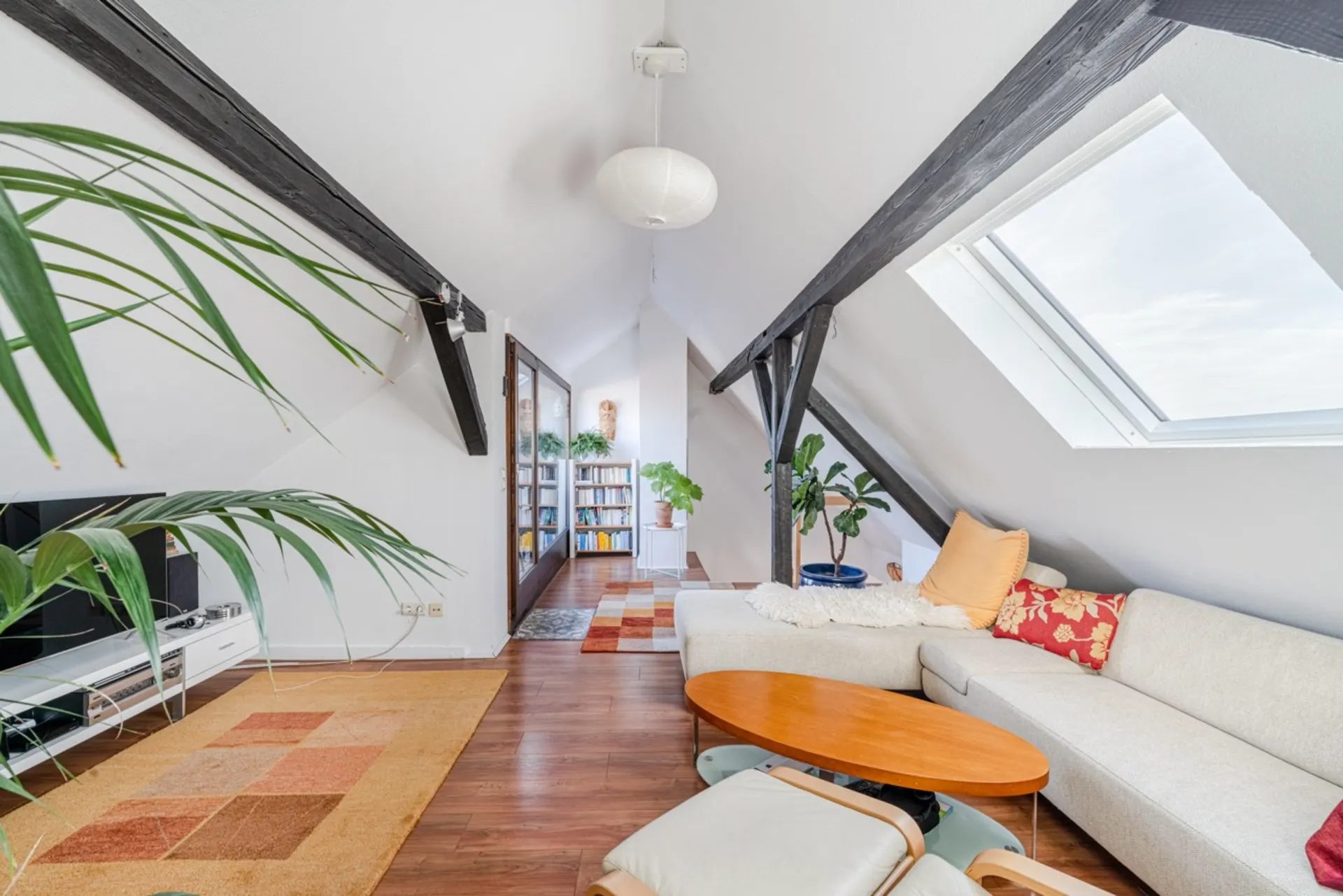 Heller Dachwohnraum mit Sofa, Holztisch, Pflanzen, Teppich und Dachfenster.
