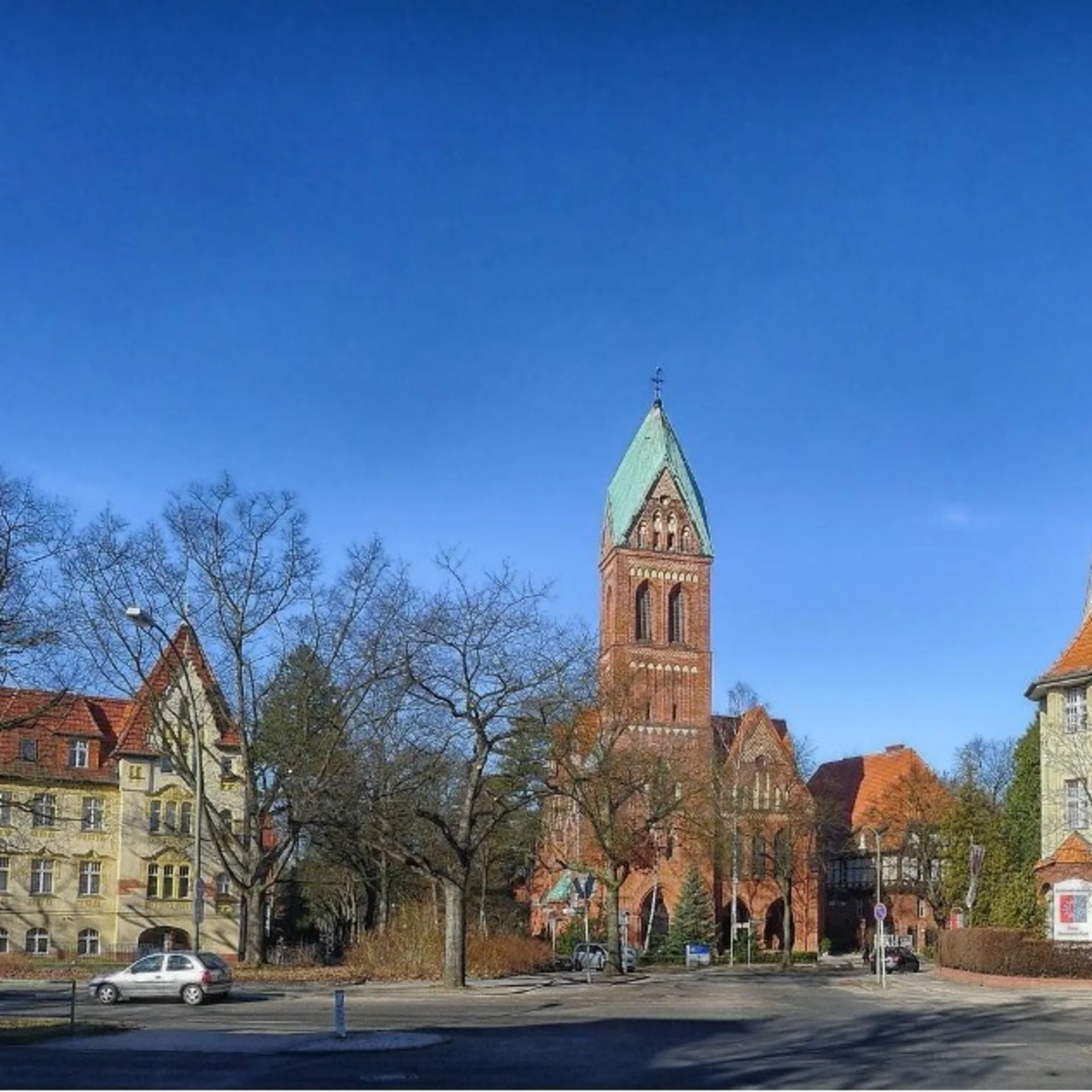 Straßenszene mit Wohnhäusern, Bäumen ohne Laub und einer großen Kirche im Hintergrund.