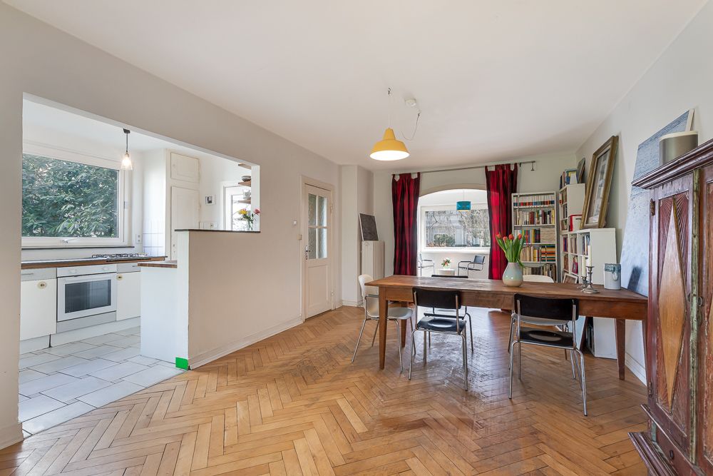 Helles Esszimmer mit Holzboden, großem Tisch, Bücherregal und Blick in die offene Küche.