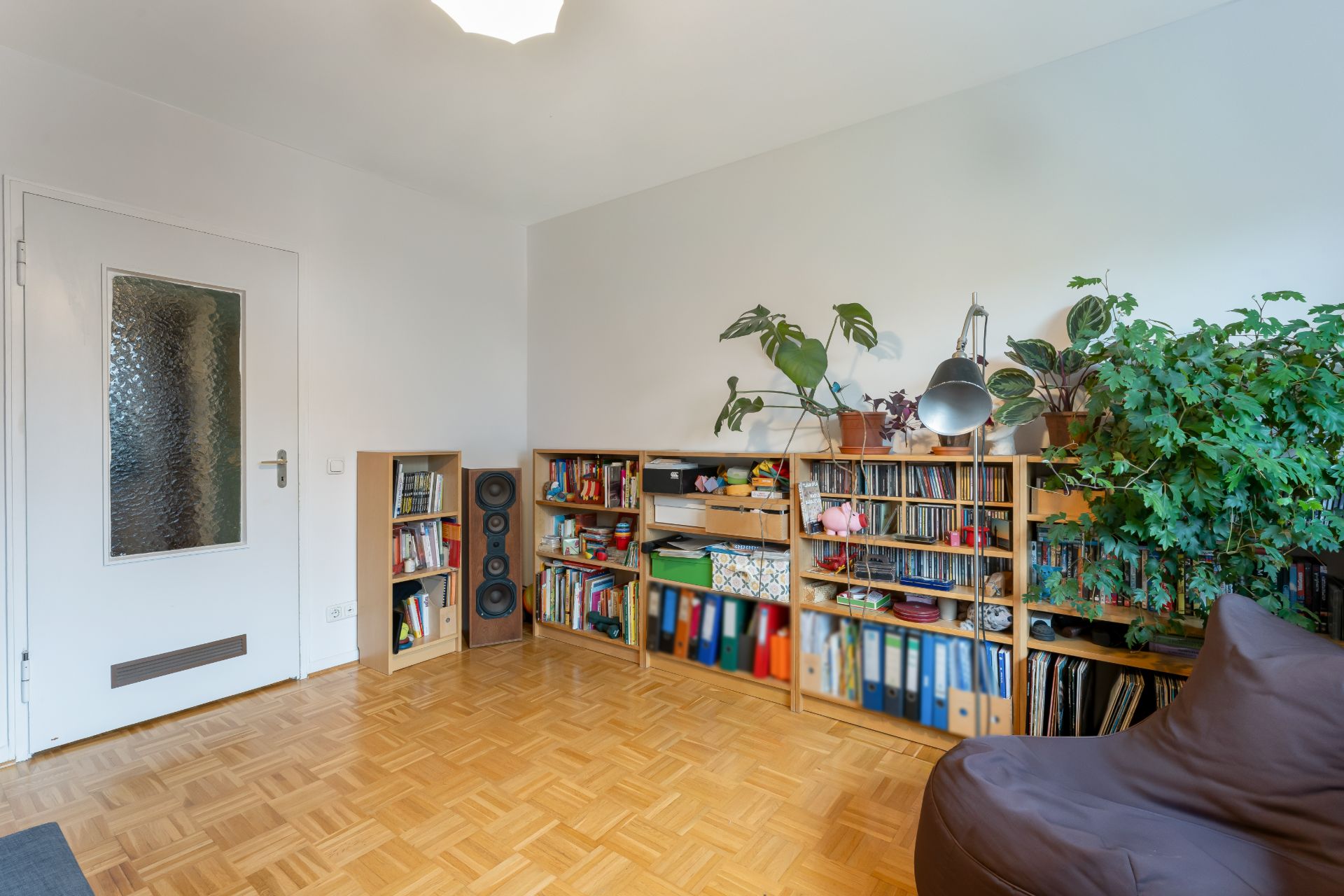 Wohnzimmer mit Bücherregalen, Pflanzen und Sitzsack auf Parkettboden.