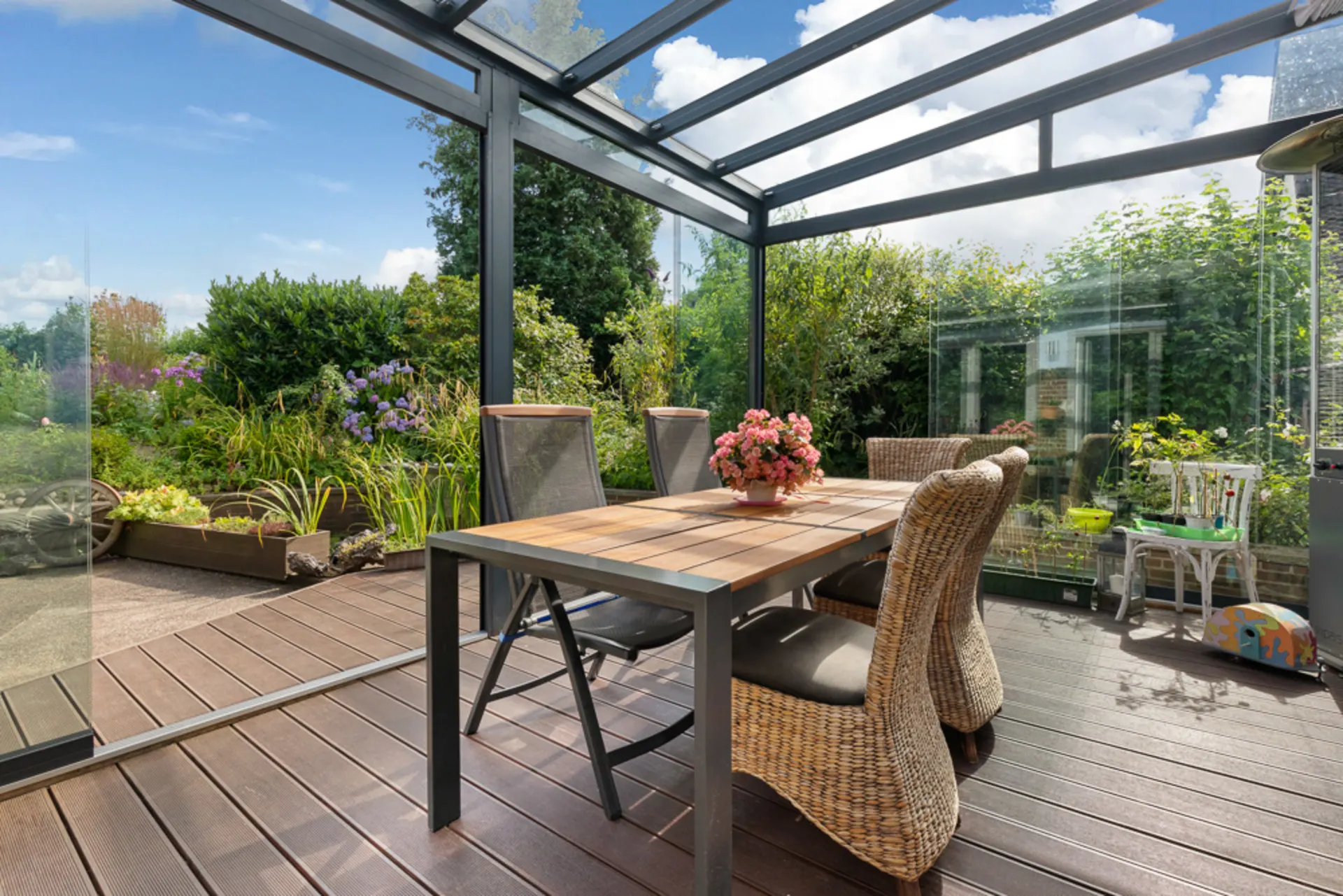 Überdachte Terrasse mit Holztisch, Stühlen und Blick auf bepflanzten Garten.