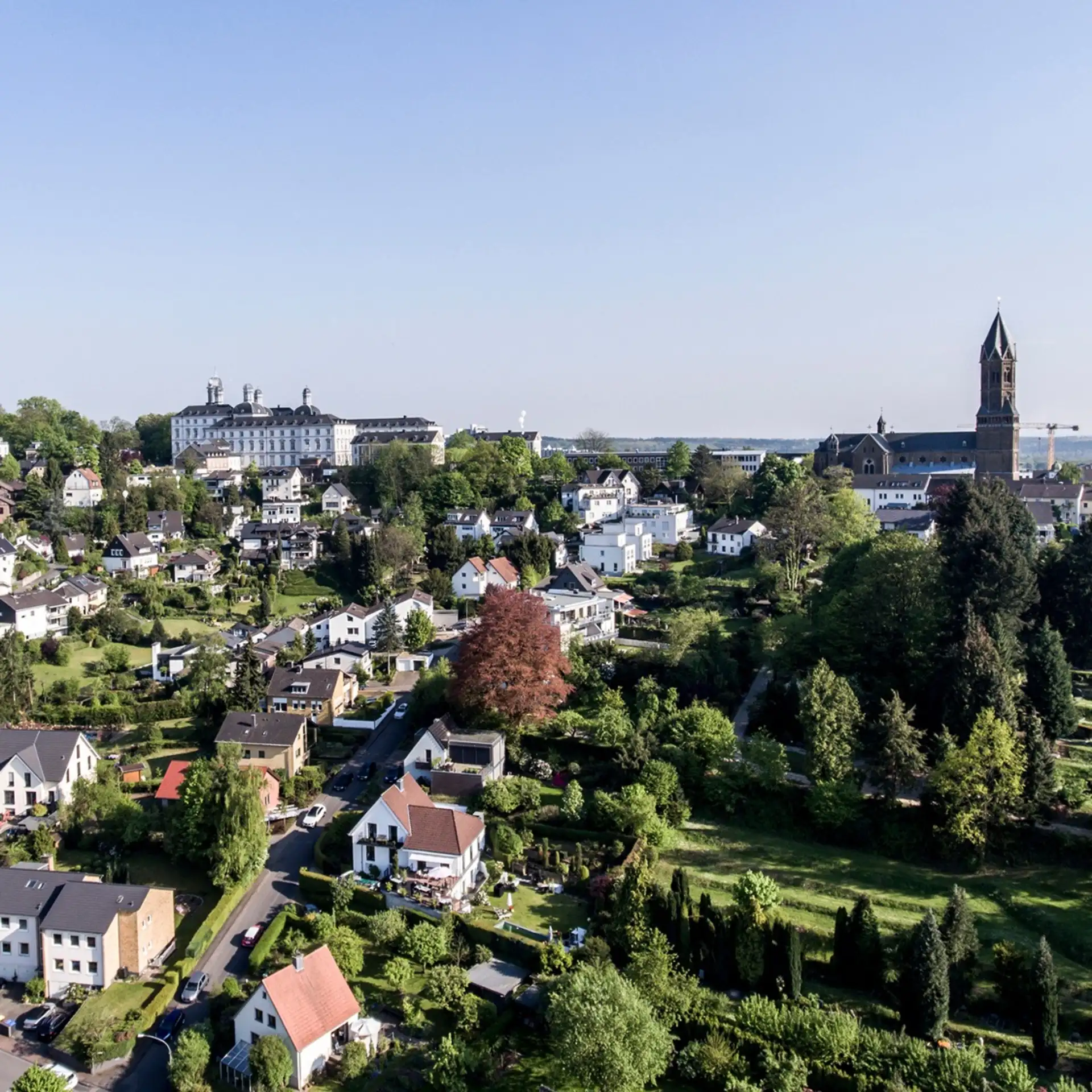 Luftaufnahme von Wohnhäusern, viel Grün und einer großen Kirche im Hintergrund.