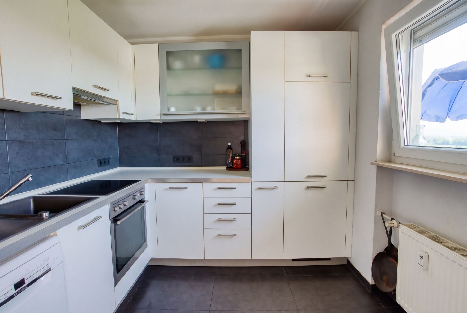 Moderne Küche mit weißen Schränken, Elektroherd, Spüle und offenem Fenster.