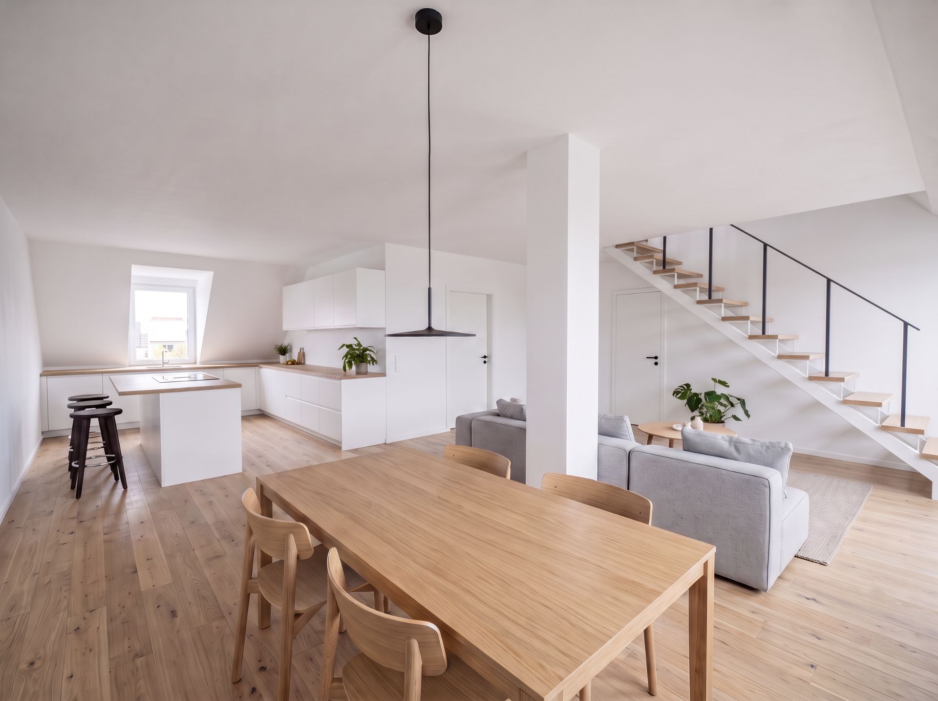 Helles Wohnzimmer mit Holzfußboden, Esstisch, Sofa, moderner Küche und Treppe nach oben.