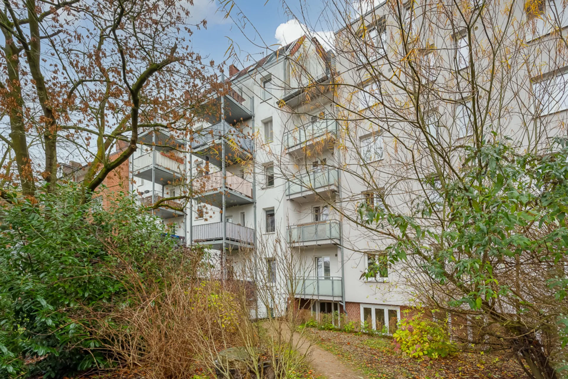 Mehrfamilienhaus mit mehreren Balkonen und Blick auf einen Garten mit Bäumen und Sträuchern.