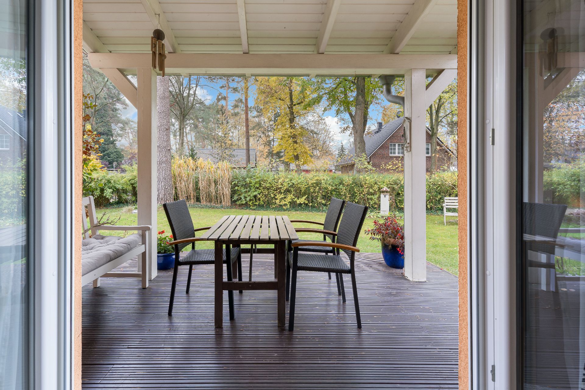 Überdachte Terrasse mit Holztisch, vier Stühlen und Gartenbank, Blick auf den Garten.