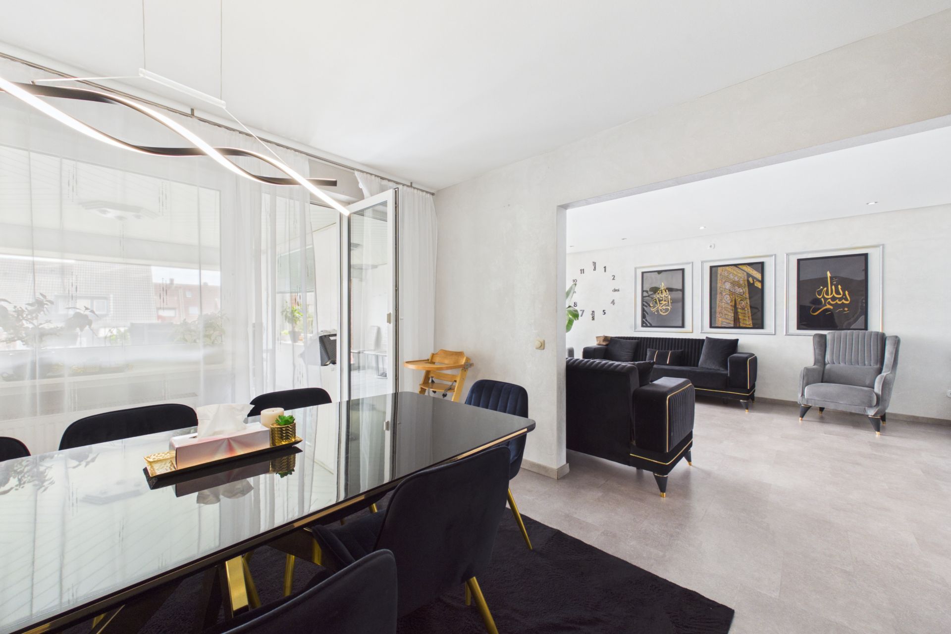 Esszimmer mit schwarzem Tisch und Stühlen, angrenzend an ein Wohnzimmer mit Sofas und Wandbildern.