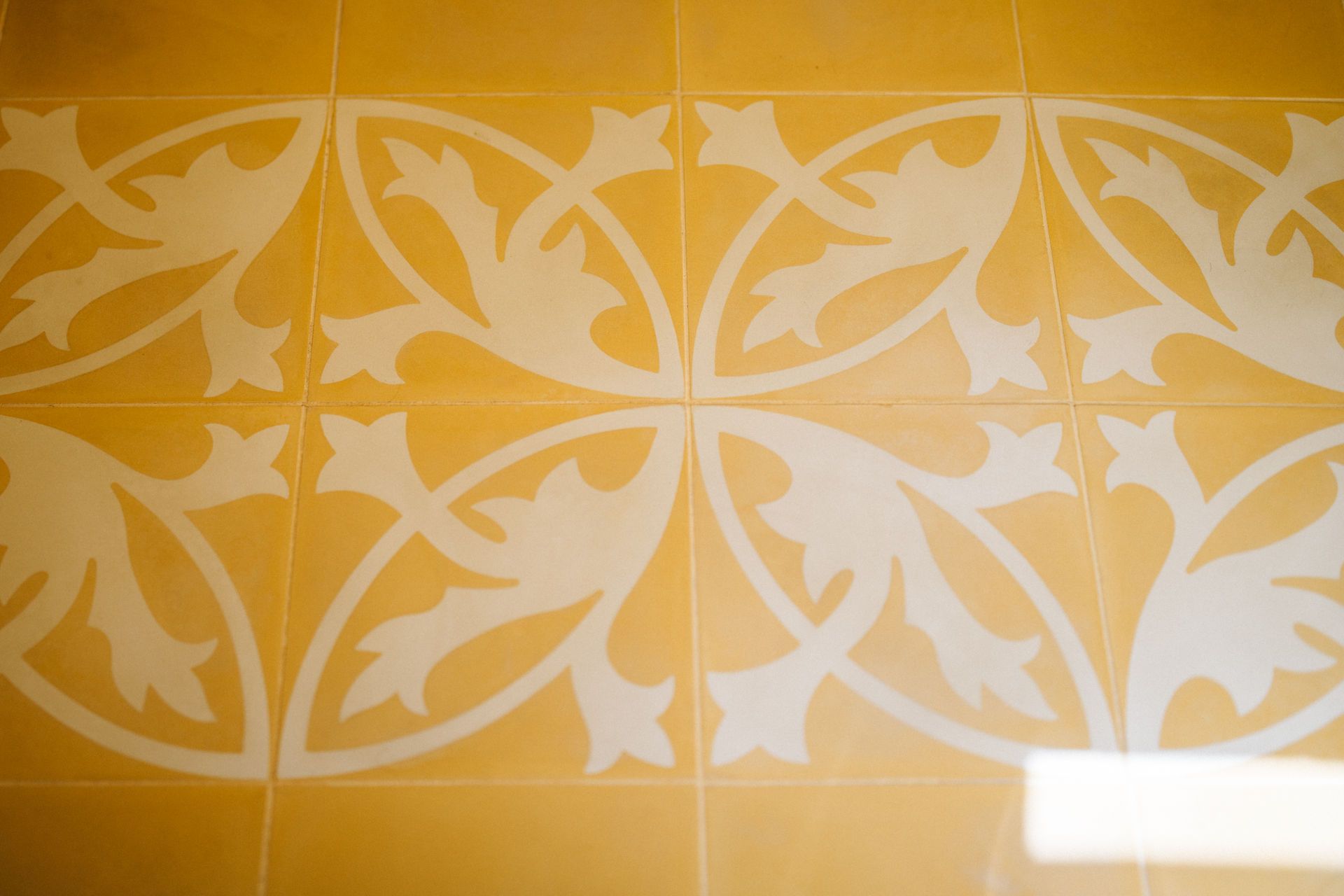 Gelbe Fliesen mit weißem, floralem Muster in sich wiederholendem Design.