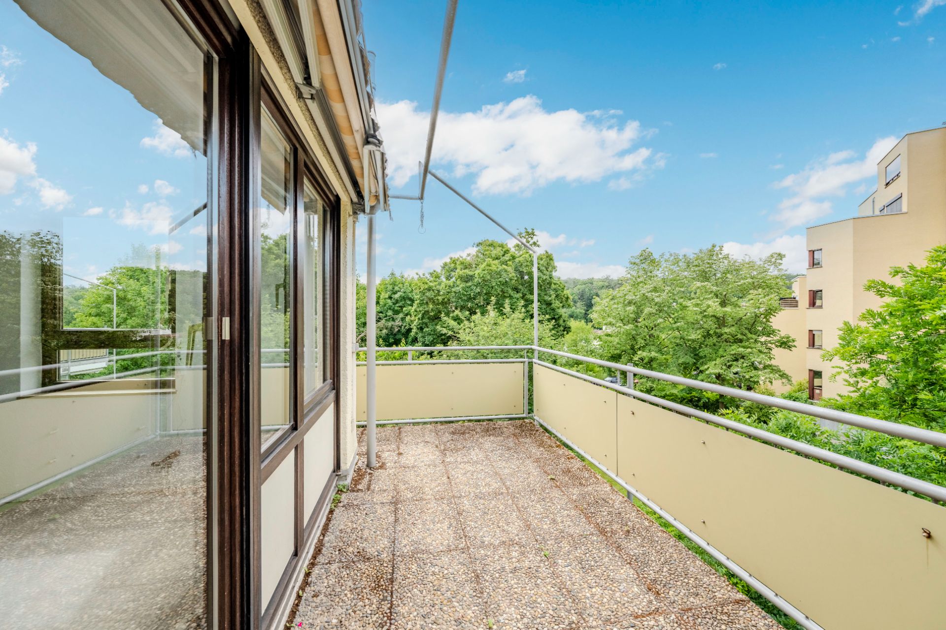 Balkon mit Geländer und Blick auf Bäume und angrenzende Gebäude.