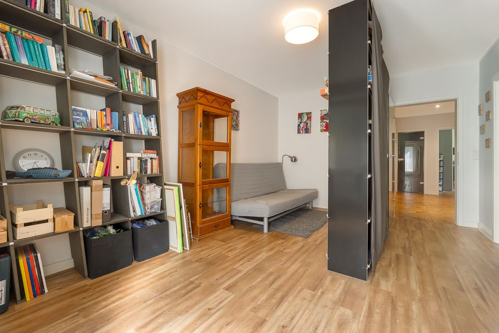 Wohnzimmer mit Bücherregal, Schlafsofa, Holzschrank und Holzboden.