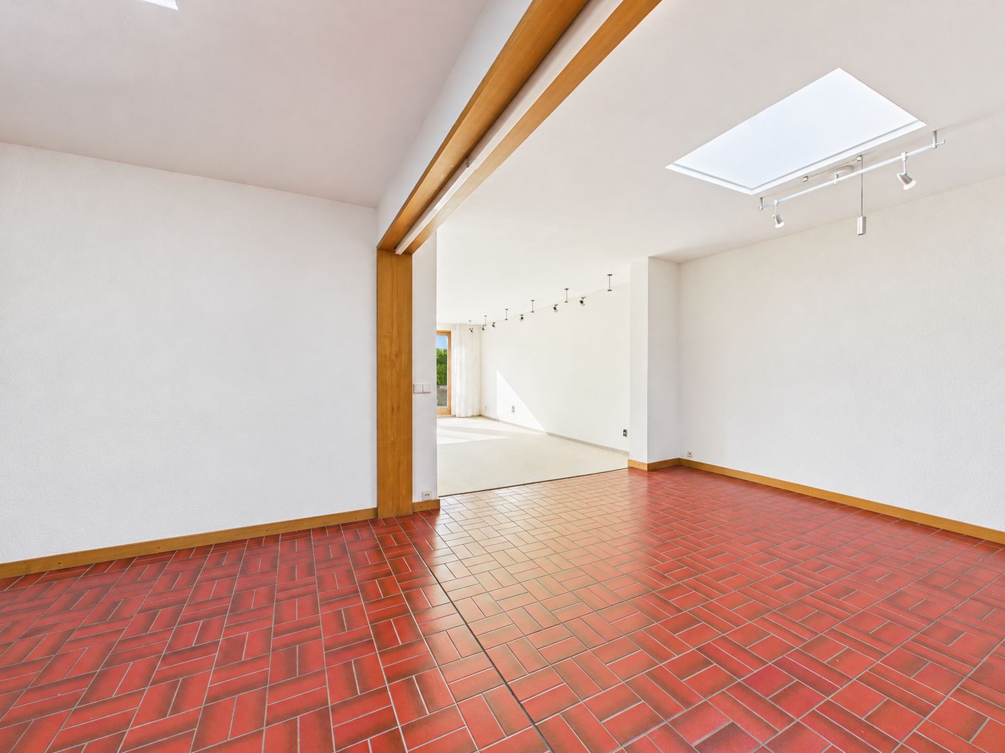 Heller Raum mit roten Fliesen, weißem Wänden und großem Dachfenster.