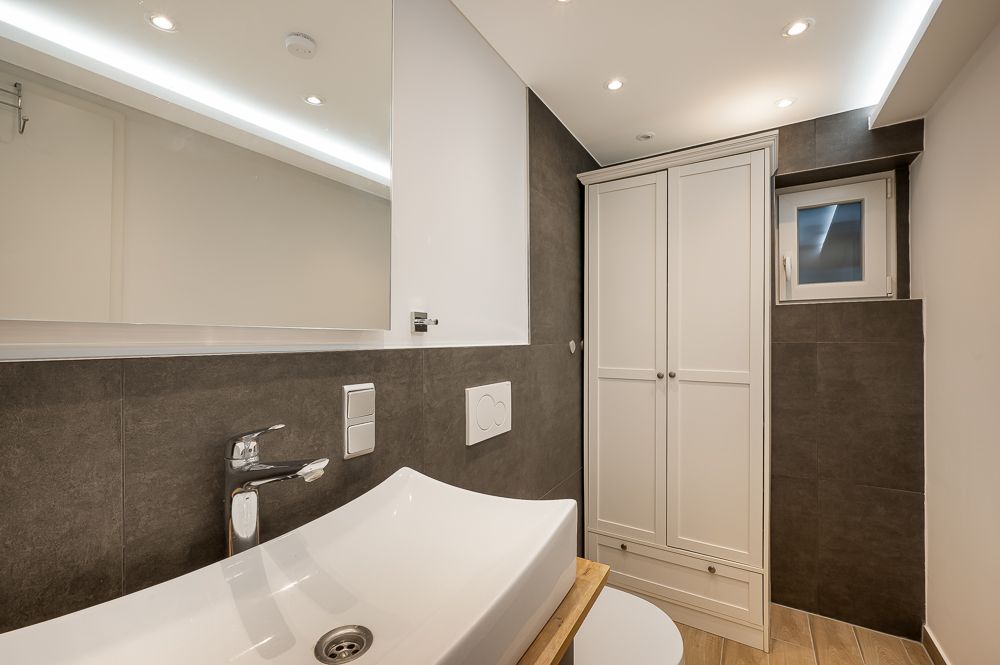 Modernes Bad mit weißem Waschbecken, Spiegel, Toilette, Schrank und kleinem Fenster.