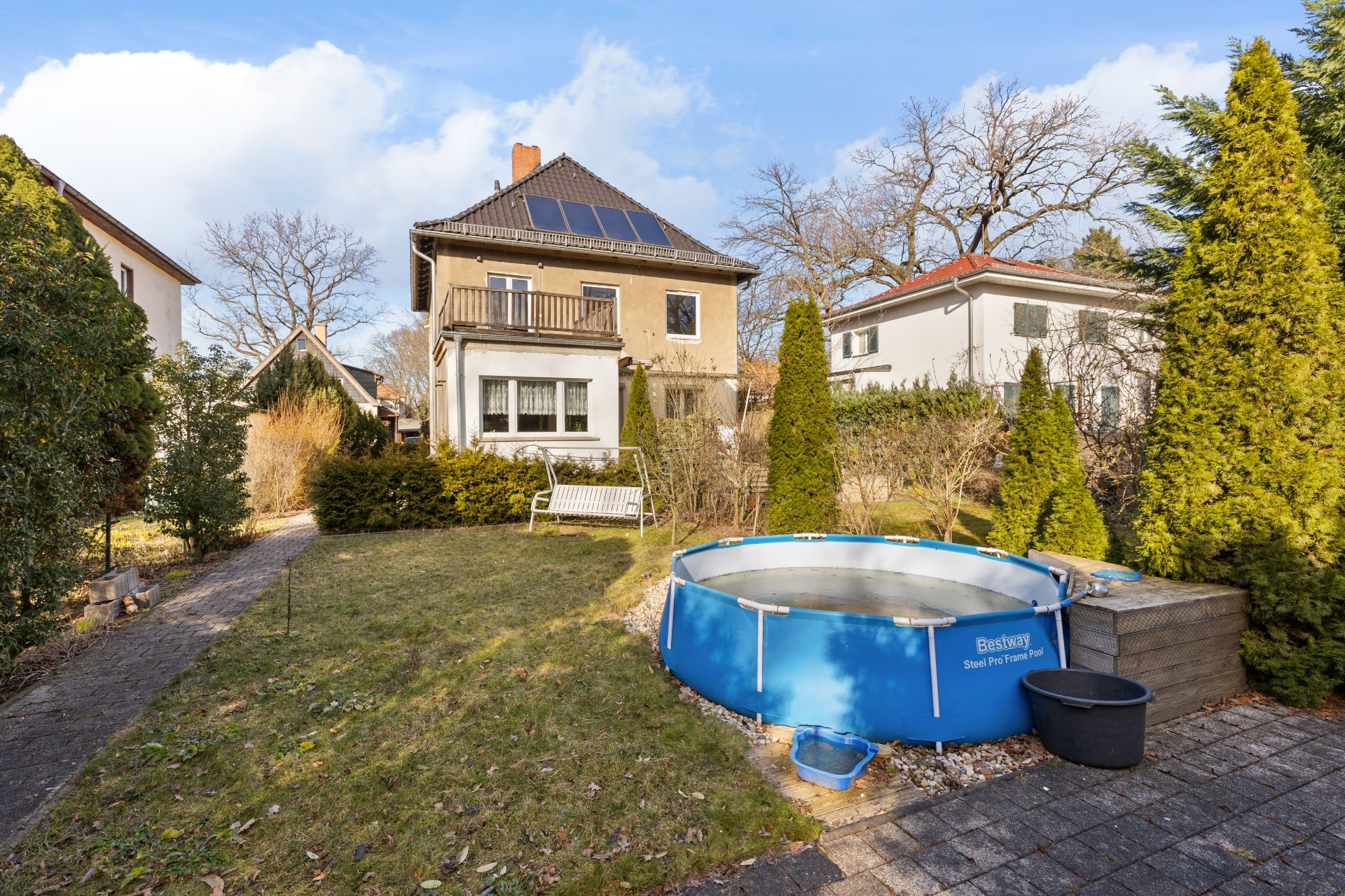 Garten mit rundem Aufstellpool, Bank, Rasen und mehrstöckigem Haus im Hintergrund.