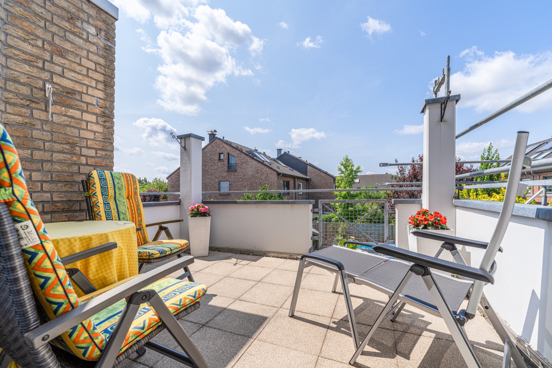 Möblierter Balkon mit zwei Stühlen, Liege und Blumenkästen, Blick auf Nachbarhäuser.
