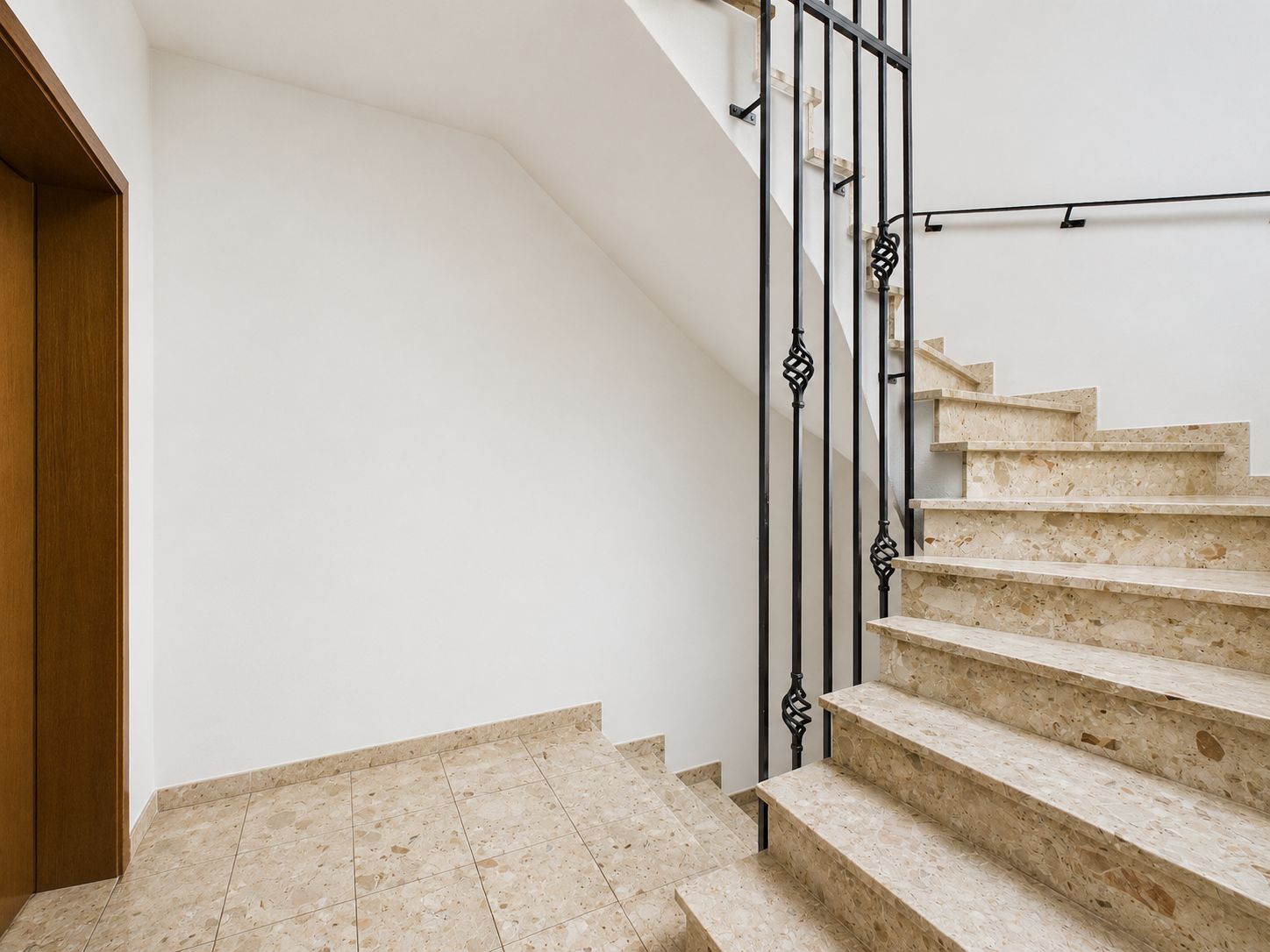Innenbereich mit Marmortreppe, schwarzem Geländer und weißer Wand.