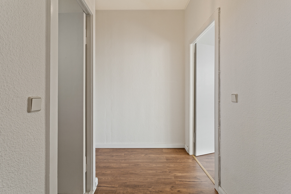 Heller Flur mit Holzboden und drei geöffneten Türen in einer Wohnung.