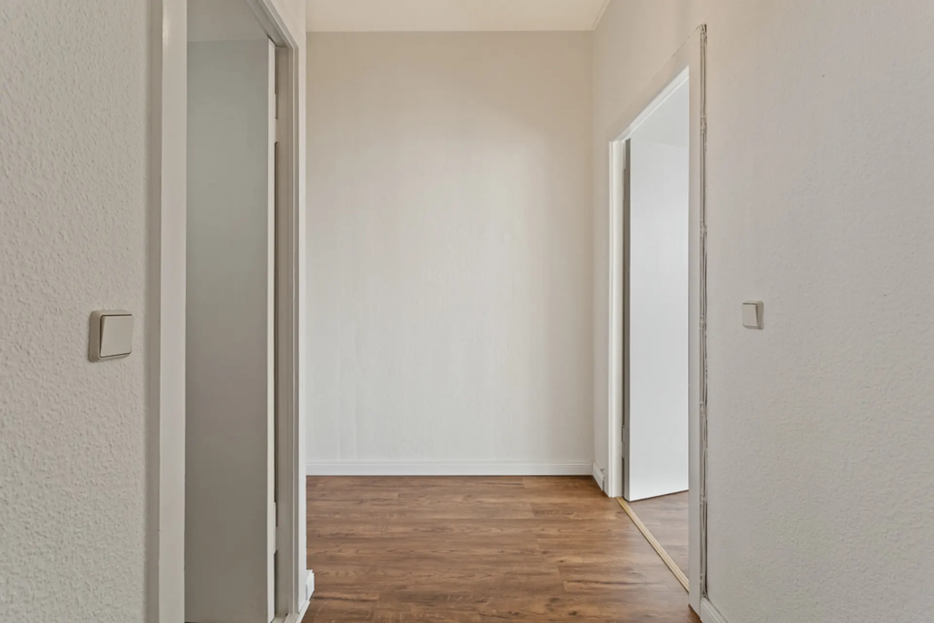 Heller Flur mit Holzboden und drei geöffneten Türen in einer Wohnung.