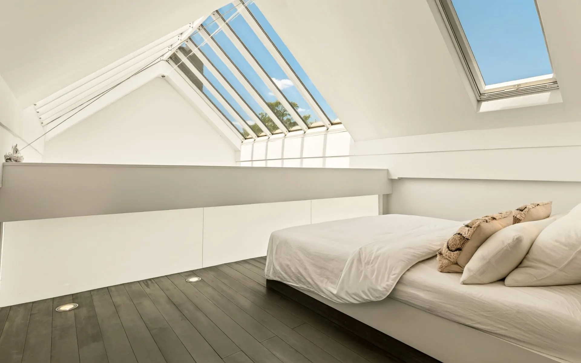 Helles Schlafzimmer mit Dachfenstern, weißem Bett und dunklem Holzboden.