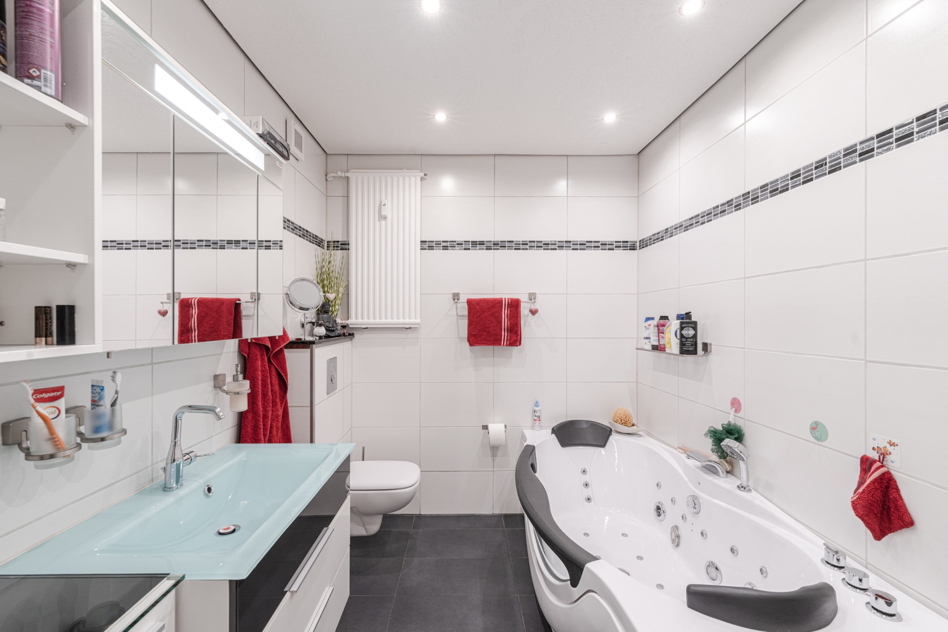 Modernes Badezimmer mit Whirlpool-Badewanne, Waschbecken, Spiegel und roten Handtüchern.