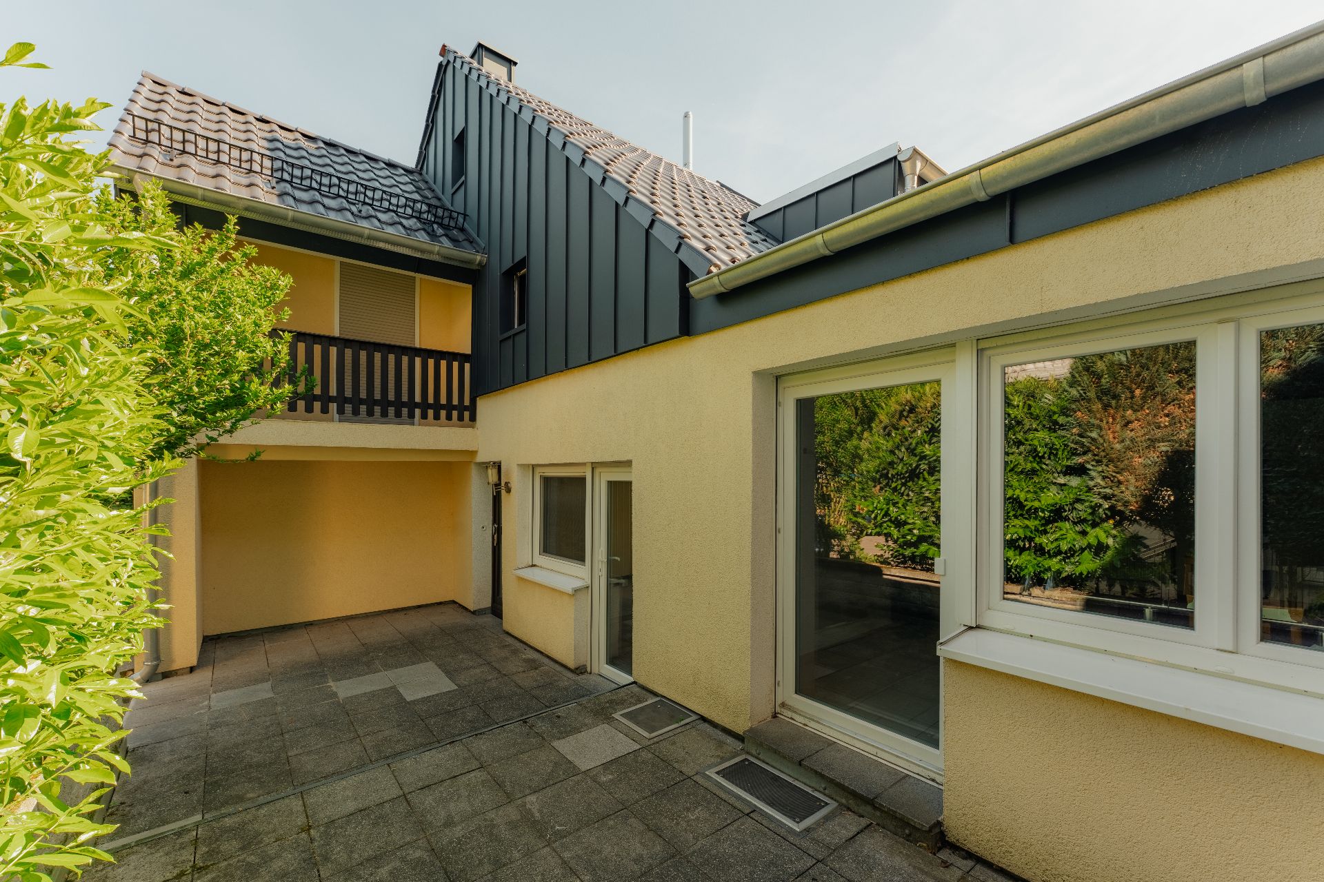 Gepflasterter Innenhof eines Wohnhauses mit Fenstern, Balkon und Gartenblick.