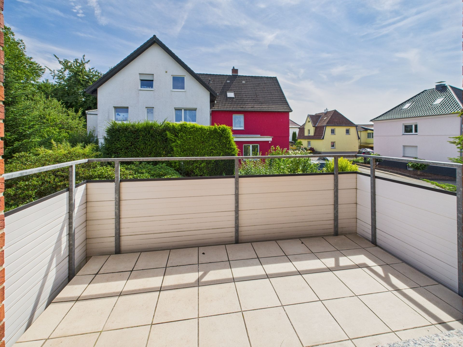 Blick von einem Balkon mit Fliesenboden auf Nachbarhäuser und grüne Büsche.