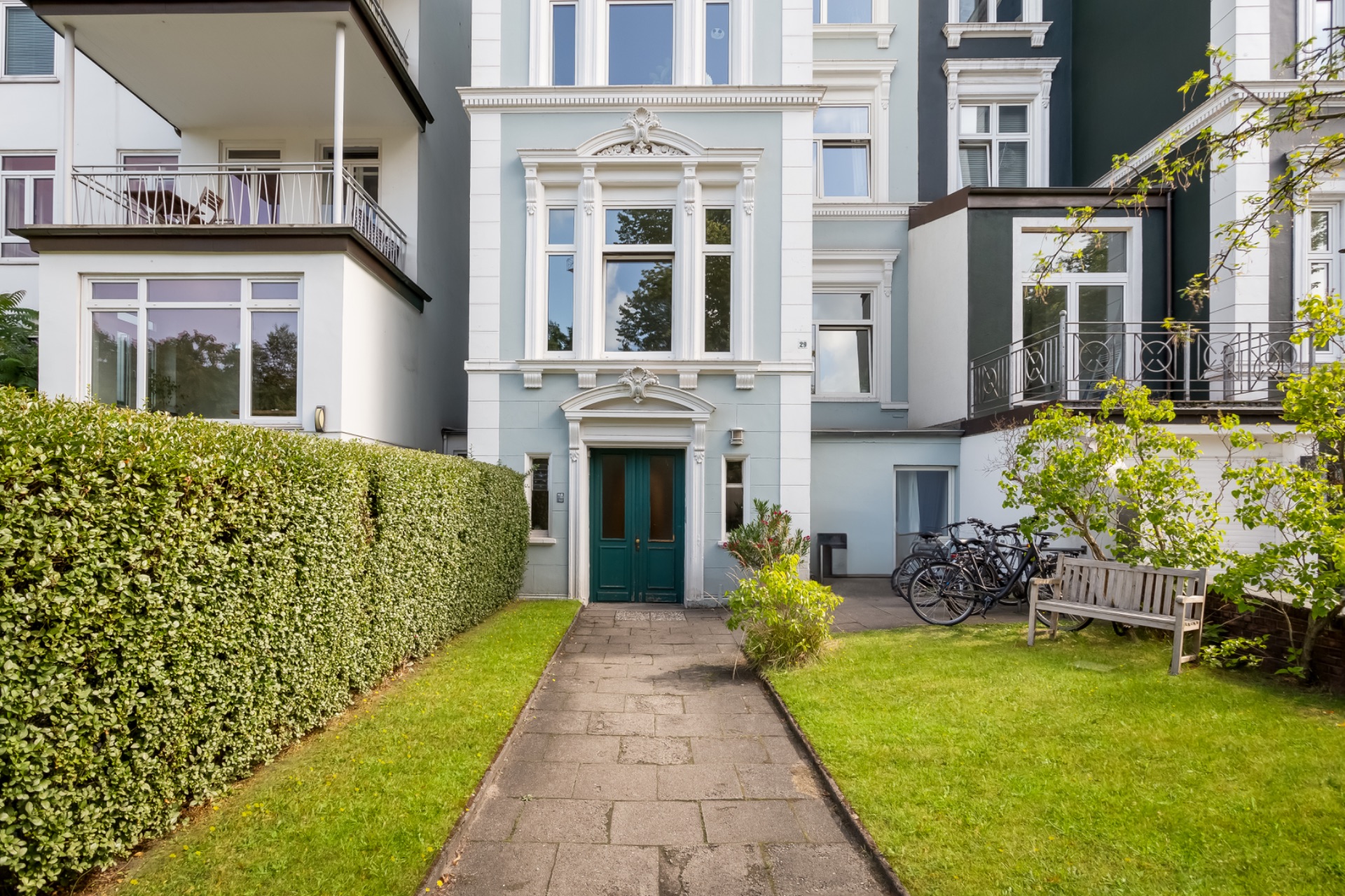 Eingang eines Wohnhauses mit grünem Tor, Gartenweg, Bank und Fahrrädern auf der rechten Seite.