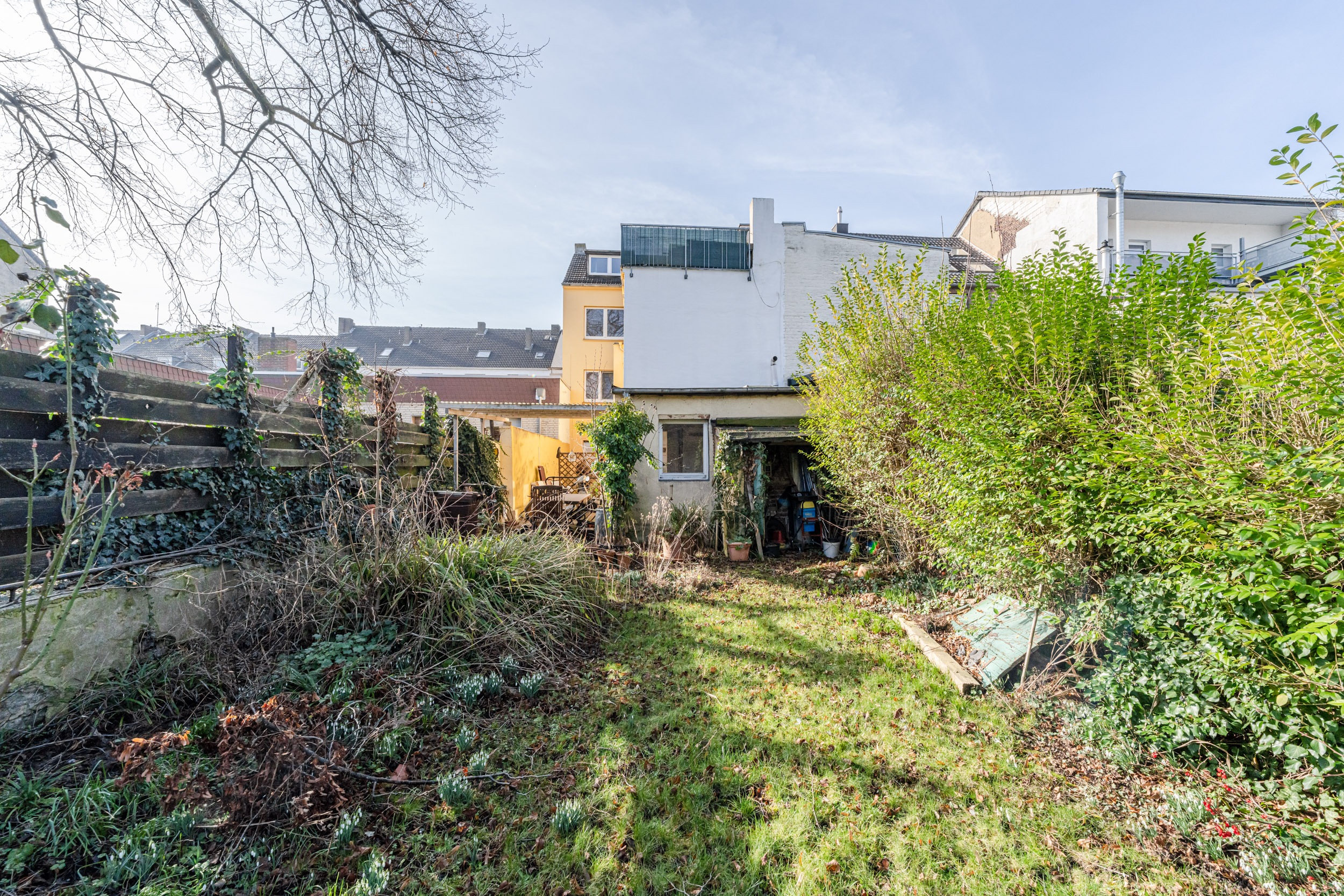 Garten mit Rasenfläche, Sträuchern und Bewuchs hinter einem Wohnhaus.