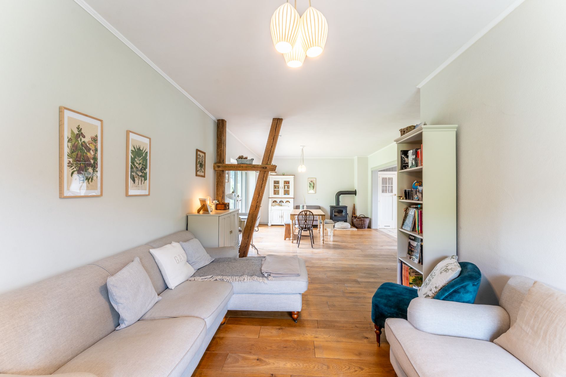 Helles Wohnzimmer mit Sofa, Holzfußboden, Esstisch, Regal und Kaminofen.