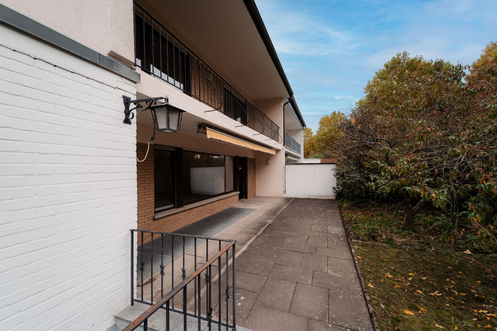 Eingangsbereich eines Wohnhauses mit Terrasse, Geländer und angrenzendem Garten.