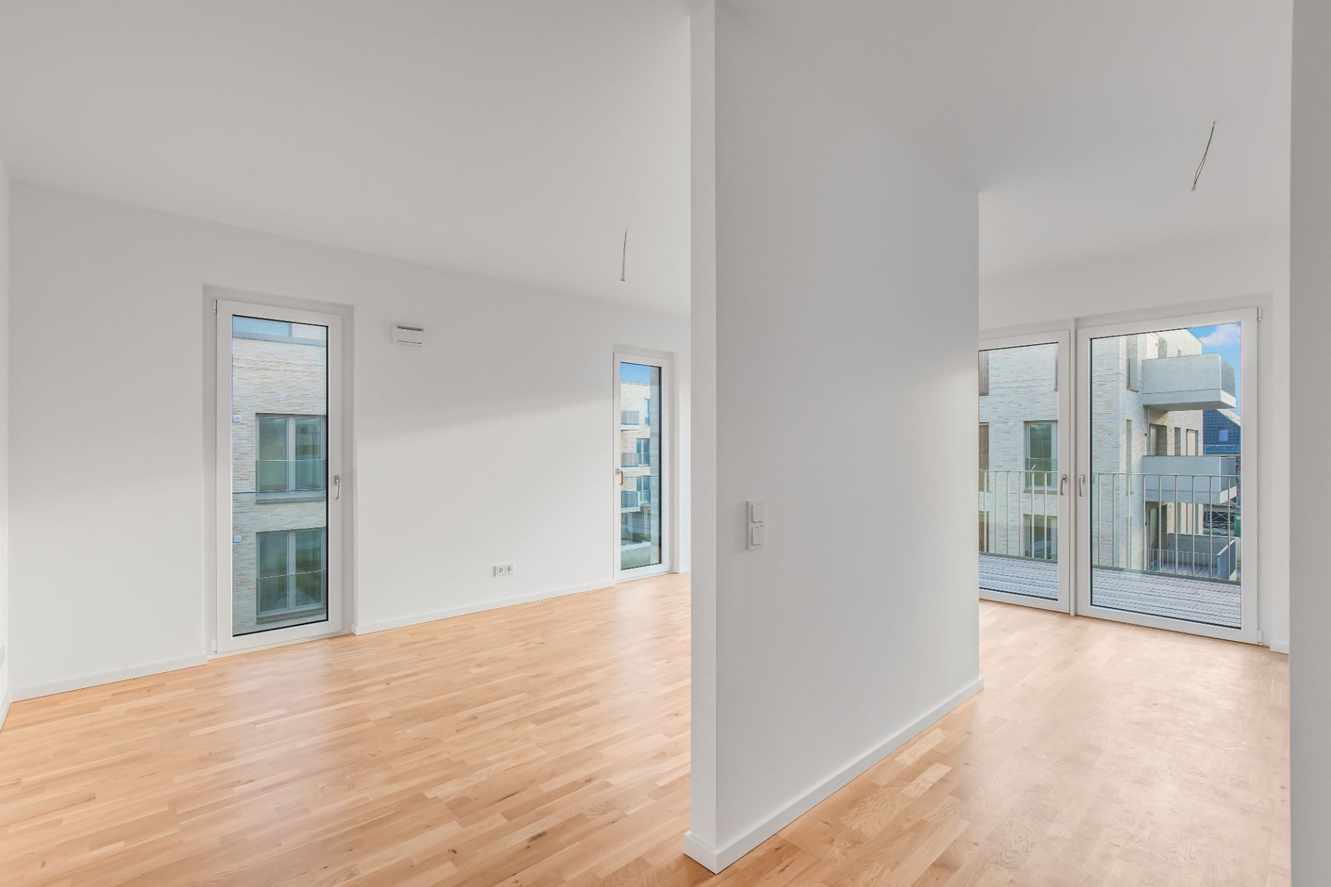 Helle, leere Wohnung mit Parkettboden und großen Fenstern.