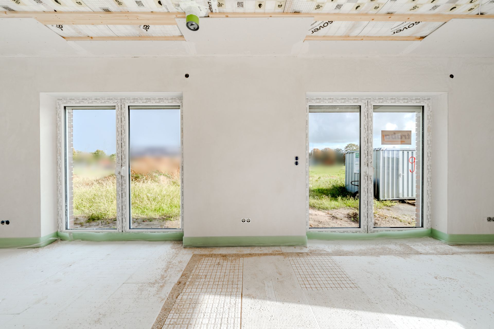 Heller Raum mit zwei großen Fenstertüren, Blick nach draußen auf Grünfläche.