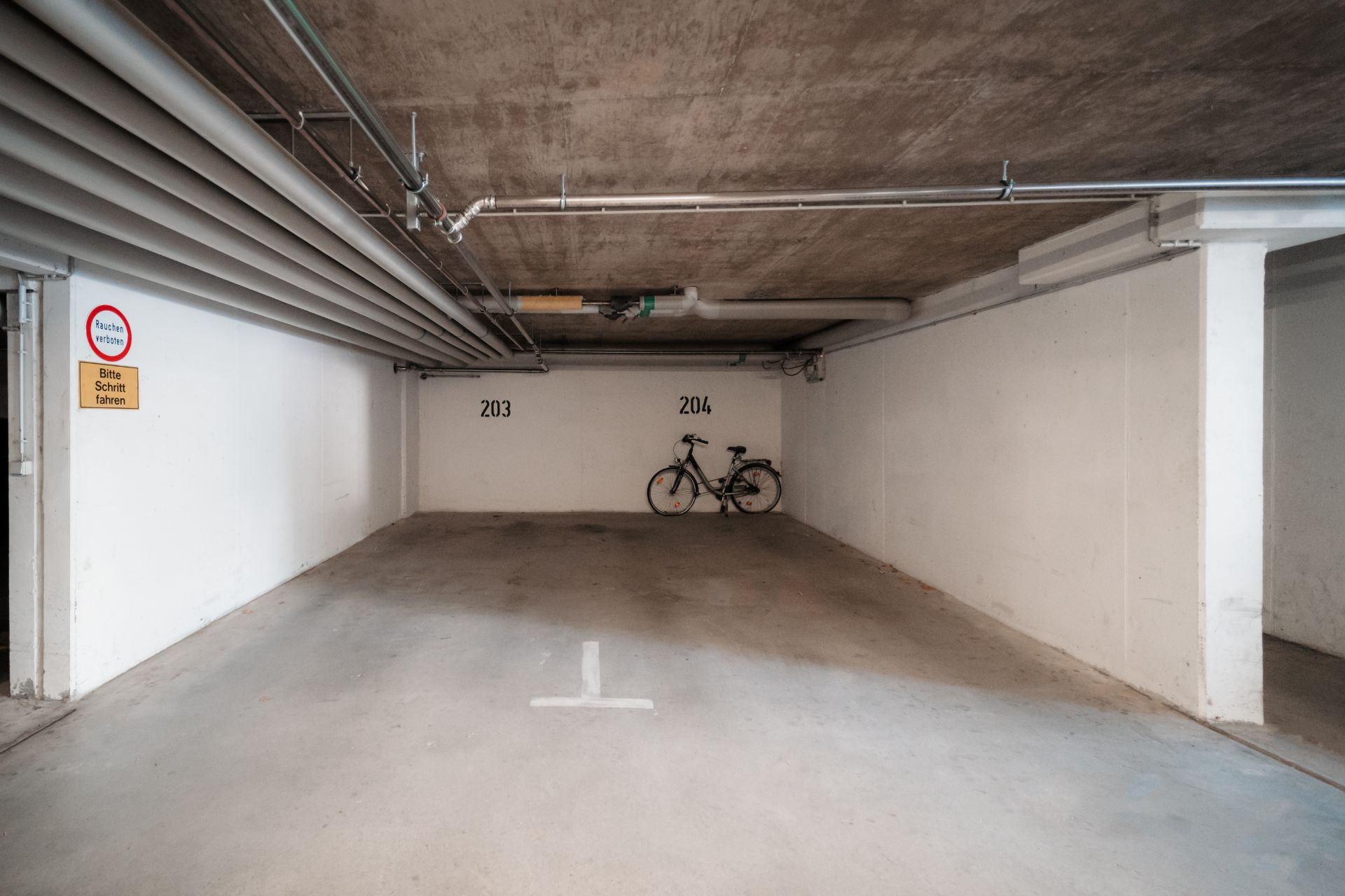 Tiefgaragenstellplatz mit einem Fahrrad an der Wand, Markierungen 203 und 204 sichtbar.
