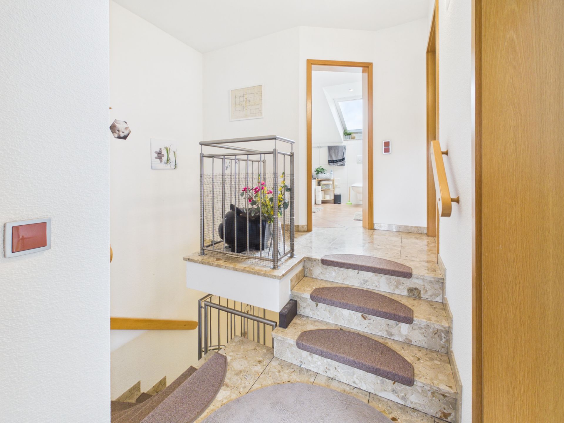 Helle Steintreppe mit Teppichstufen, Geländer, Blumen und Blick in ein helles Zimmer.