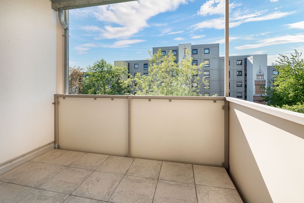 Überdachter Balkon mit Fliesenboden, Blick auf Bäume und ein Wohngebäude im Hintergrund.