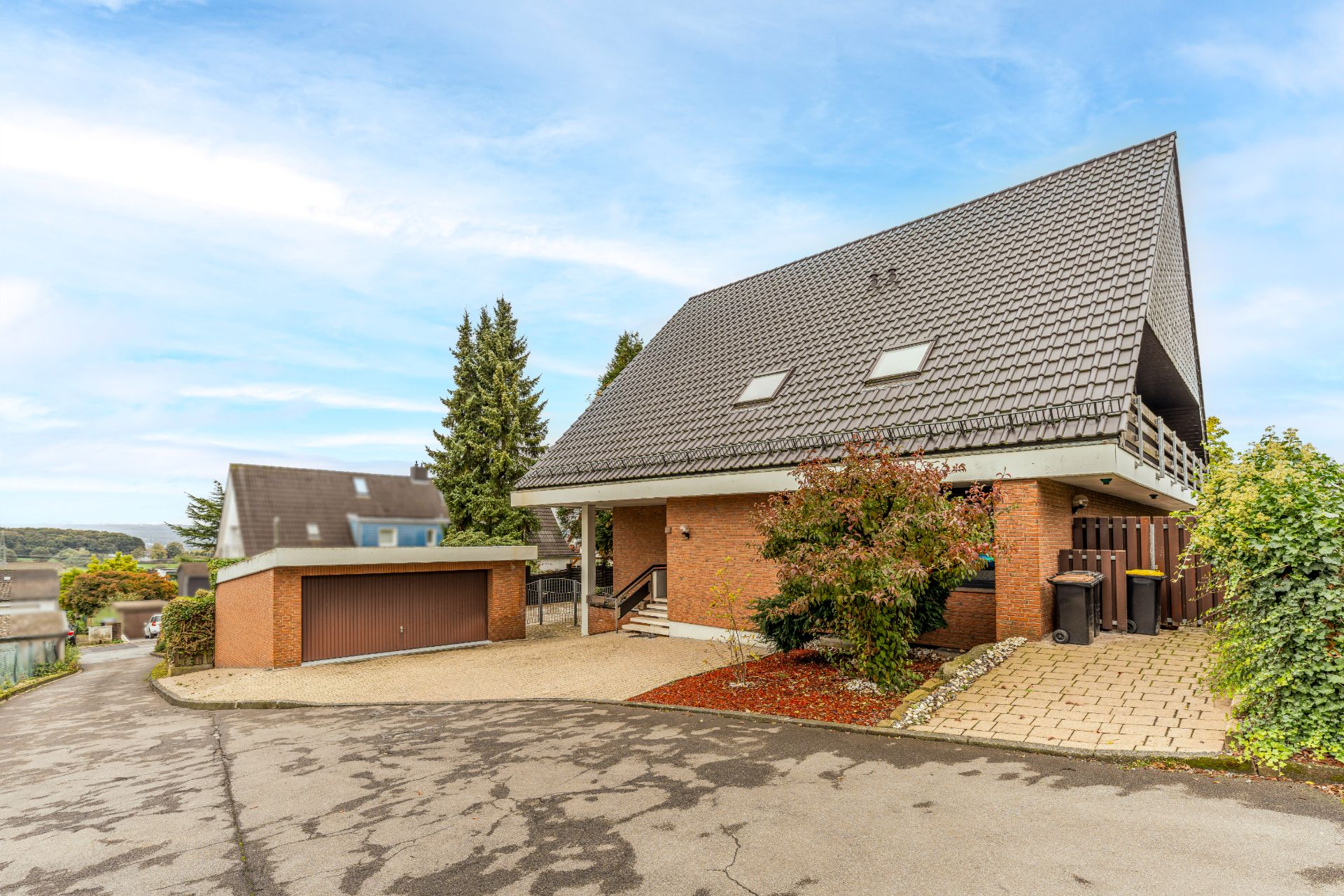 Modernes Einfamilienhaus mit steilem Dach, Garage und Vorgarten an einer Straße.