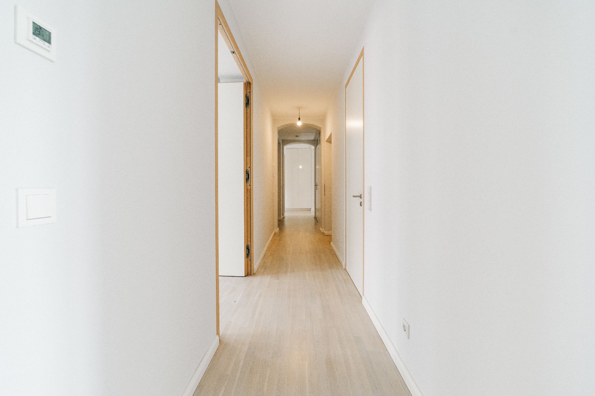 Langer, heller Flur mit Holzboden und weißen Wänden in einer Wohnung.