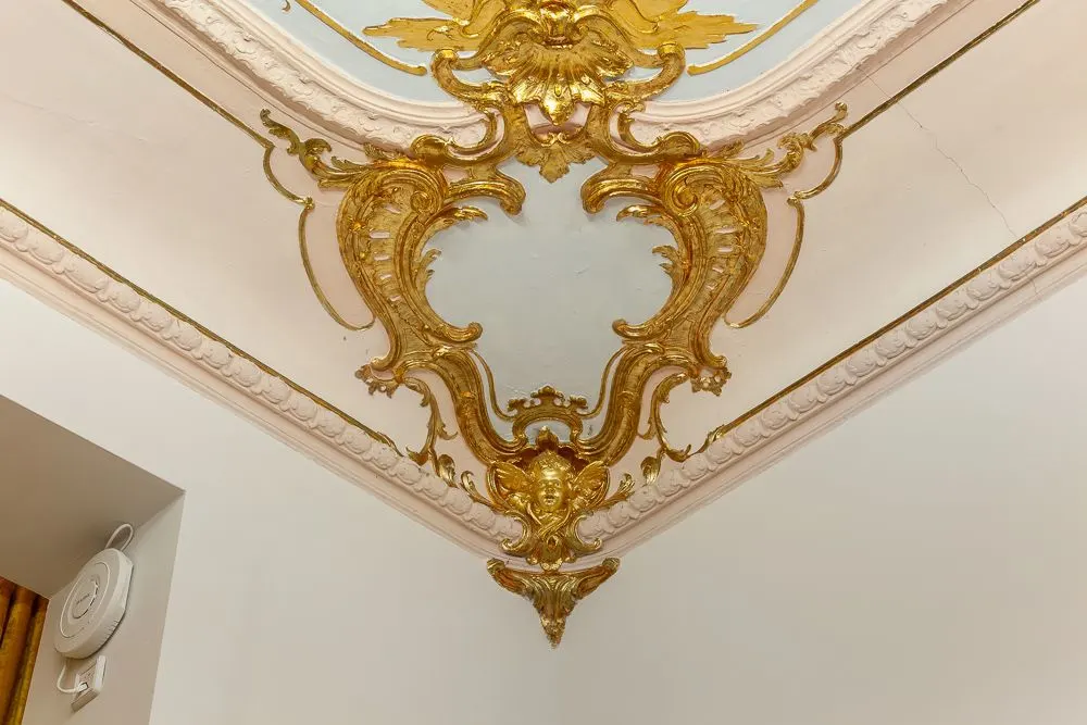 Reich verzierte Stuckdecke mit goldenen Elementen in einer Zimmerecke.