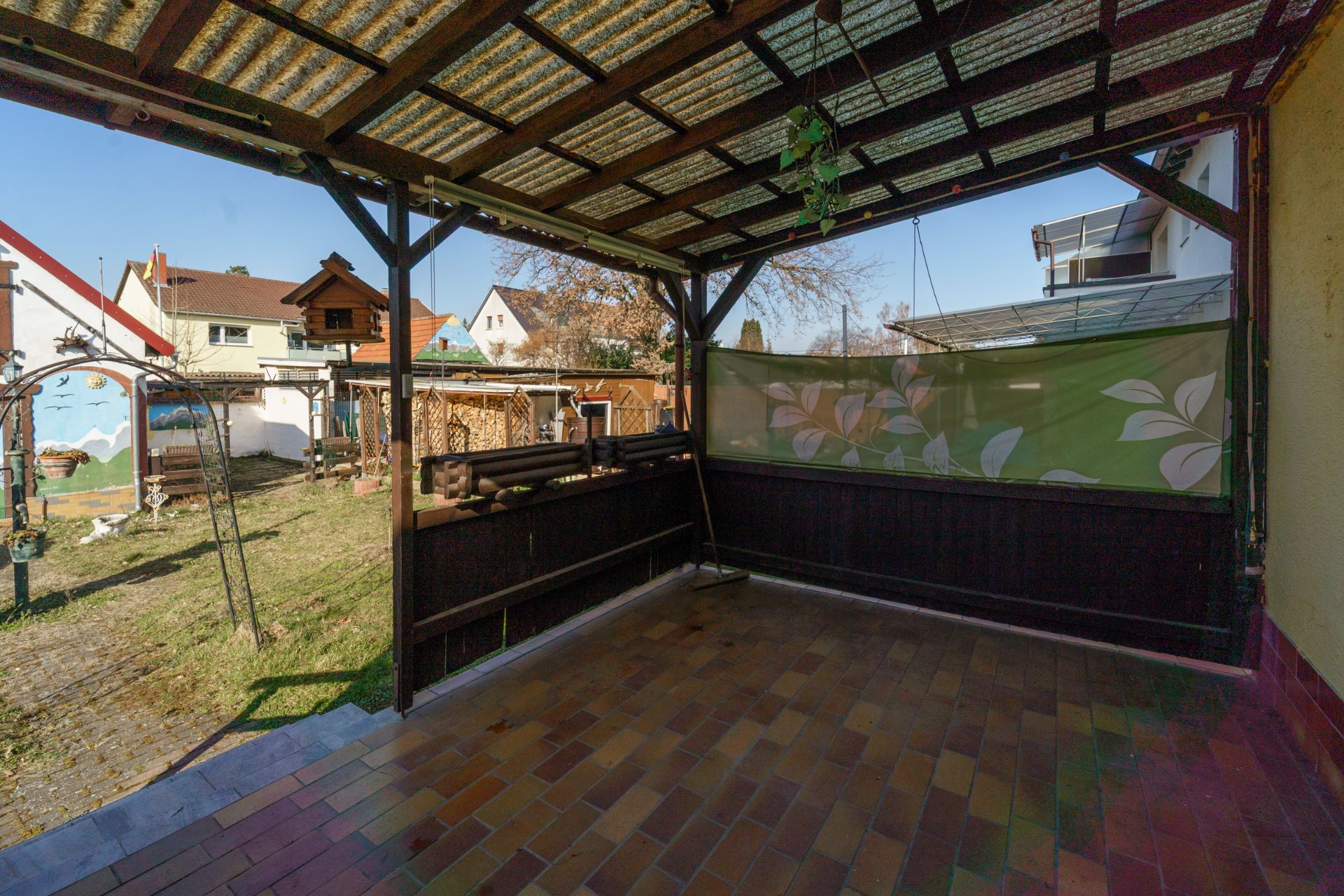 Überdachte Terrasse mit Fliesenboden und Blick auf einen Garten mit Rasen und Schaukeln.