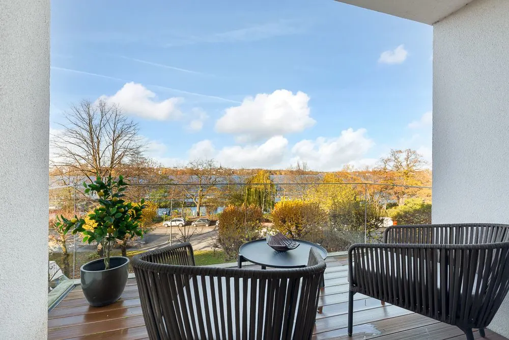 Balkon mit zwei Stühlen, Tisch und Pflanze, Blick auf Bäume und blauen Himmel.
