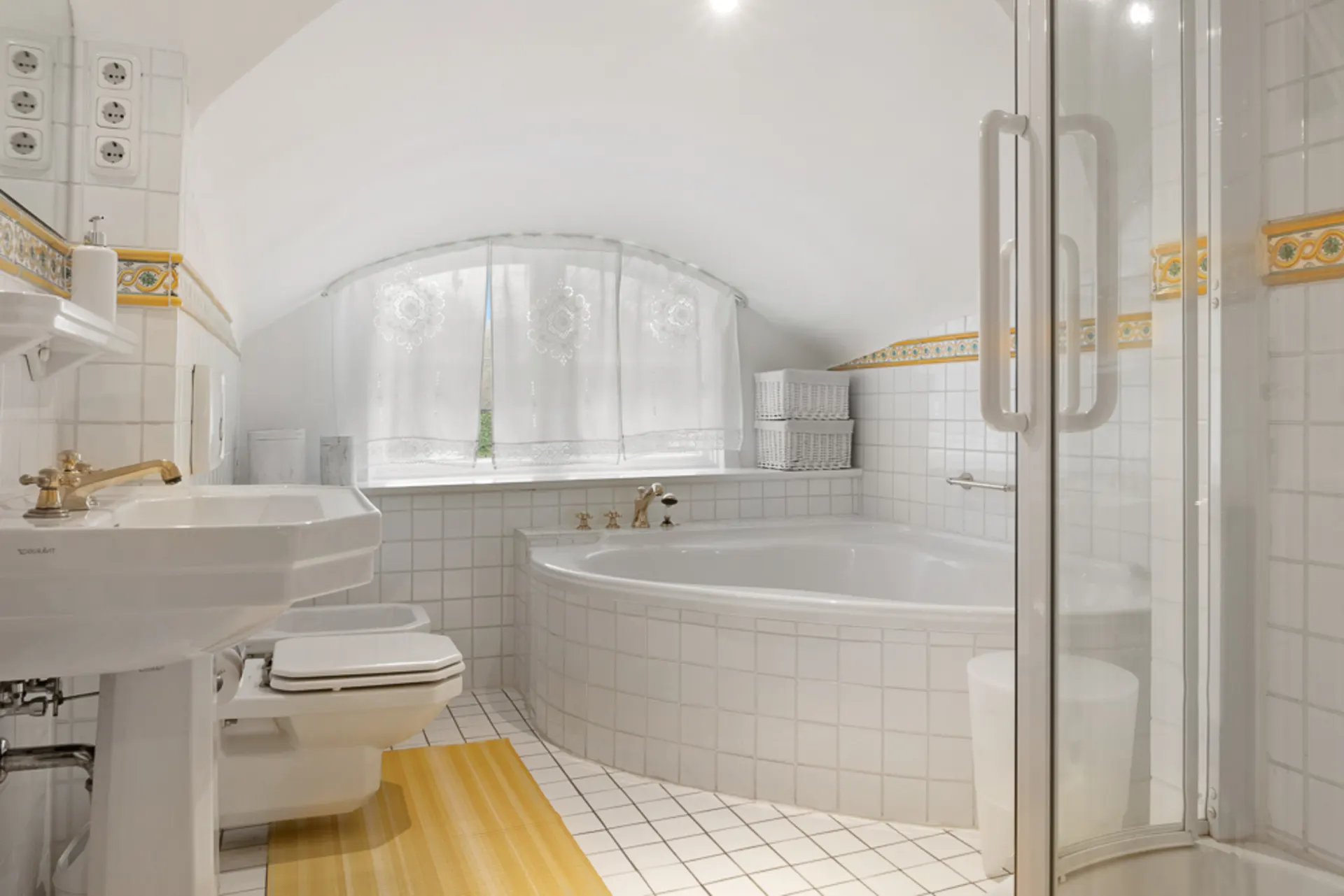 Helles Badezimmer mit Eckbadewanne, Dusche, Waschbecken und WC unter einem Rundfenster.