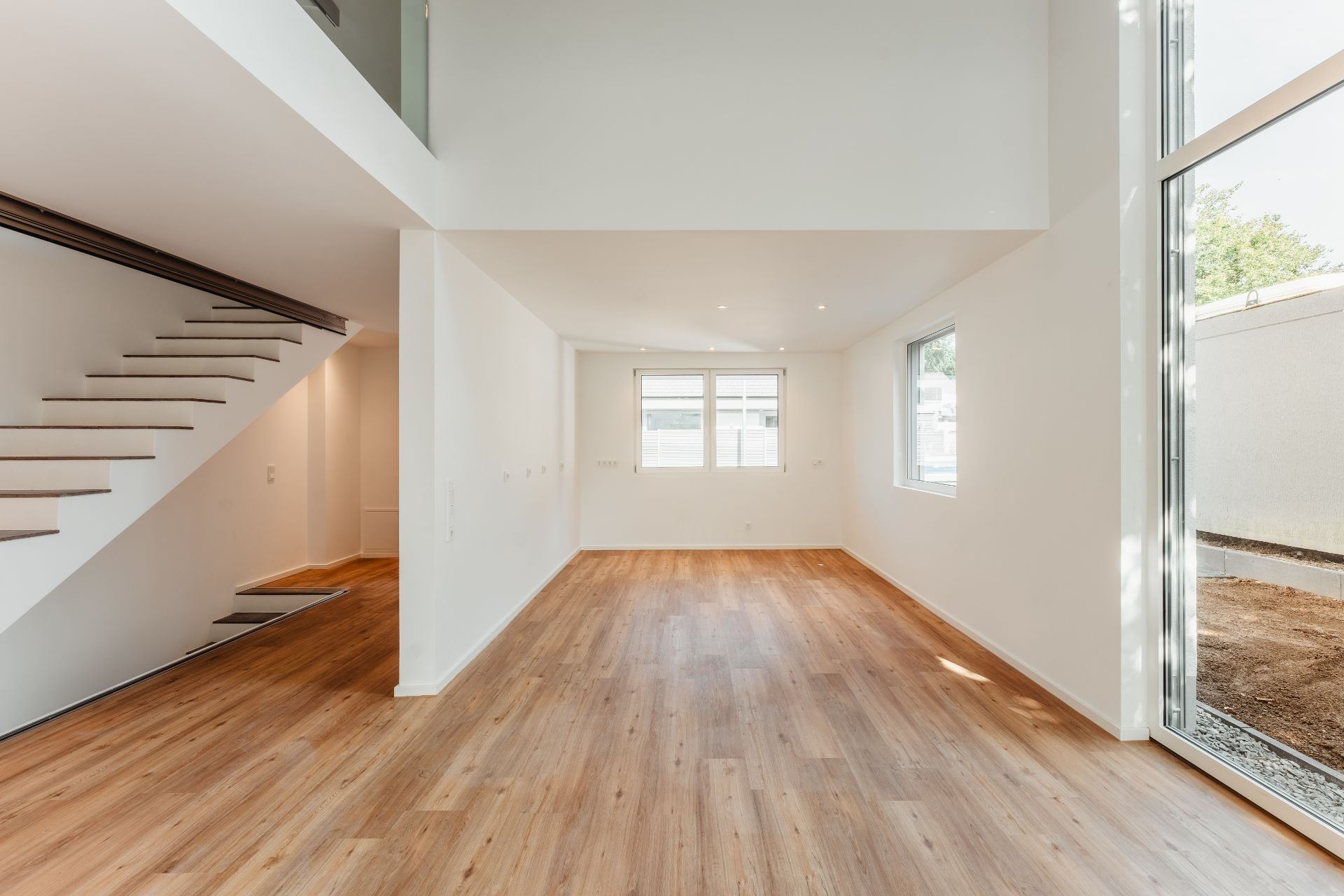 Heller, leerer Wohnraum mit Holzfußboden, weißen Wänden und einer modernen Treppe.