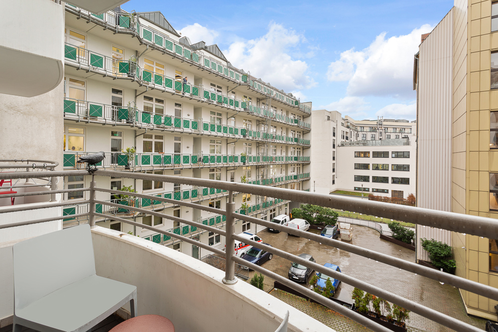 Blick von einem Balkon auf einen Innenhof mit geparkten Autos und mehrstöckigen Wohngebäuden.