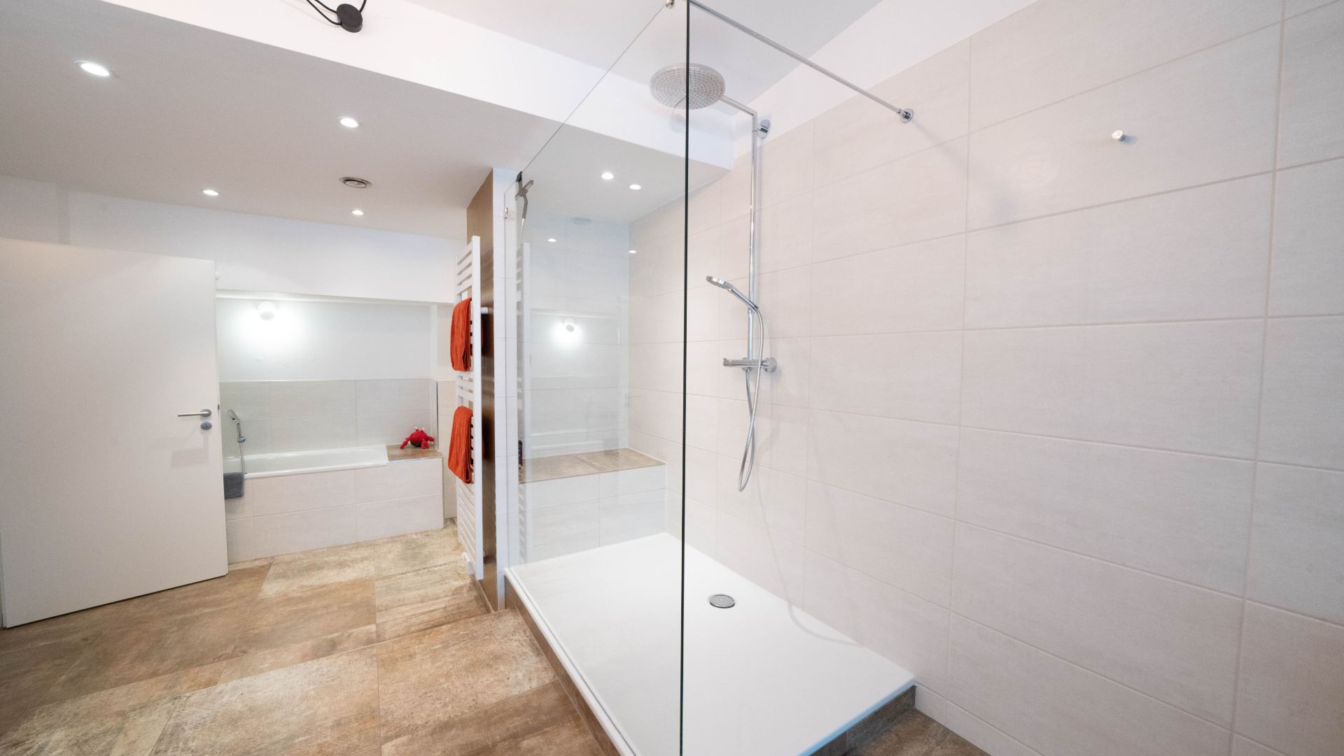 Modernes Badezimmer mit großer Dusche, Badewanne und Handtuchheizkörper mit roten Handtüchern.