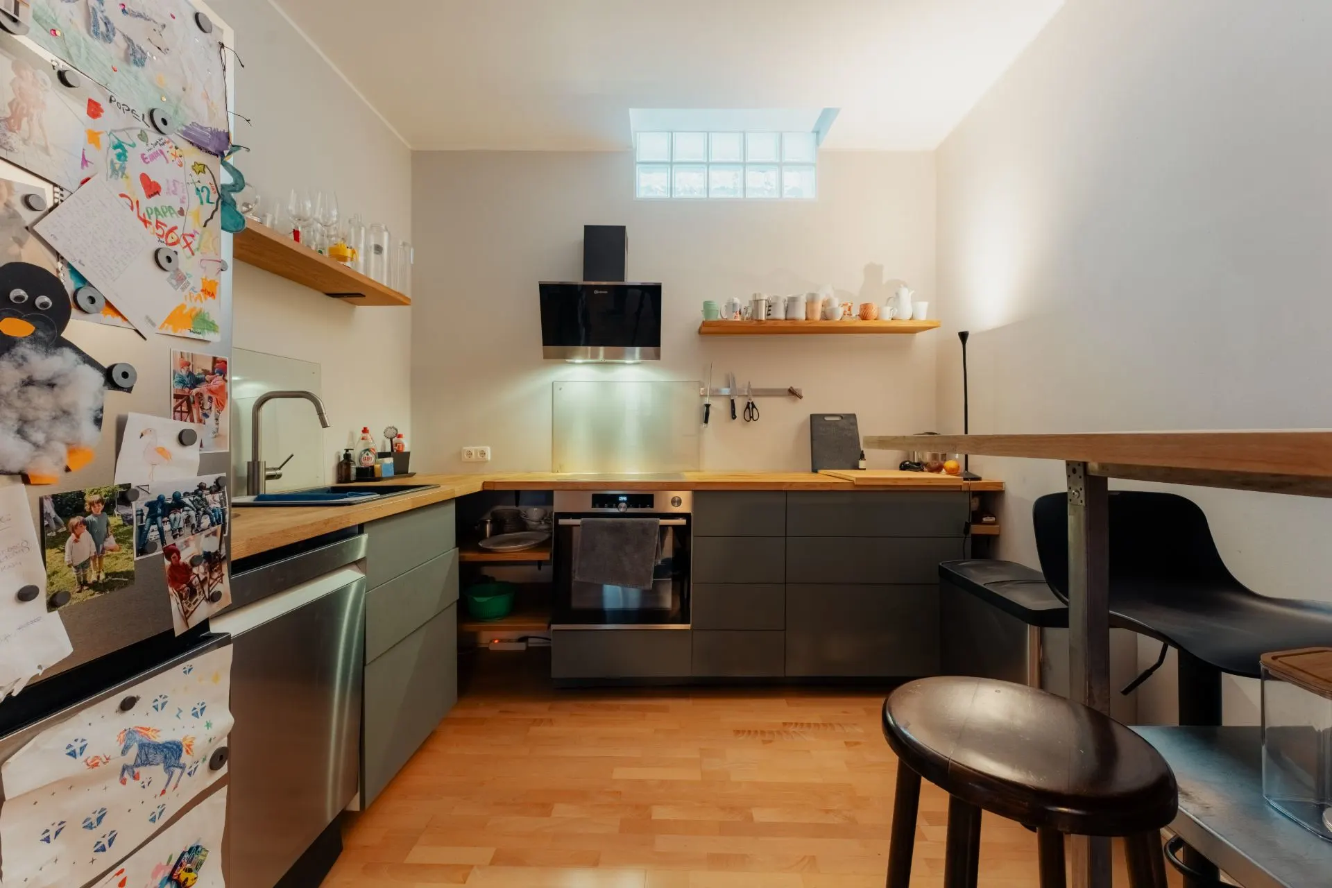 Moderne Wohnküche mit Holzboden, Kühlschrank mit Zeichnungen, Barhockern und Oberlicht.