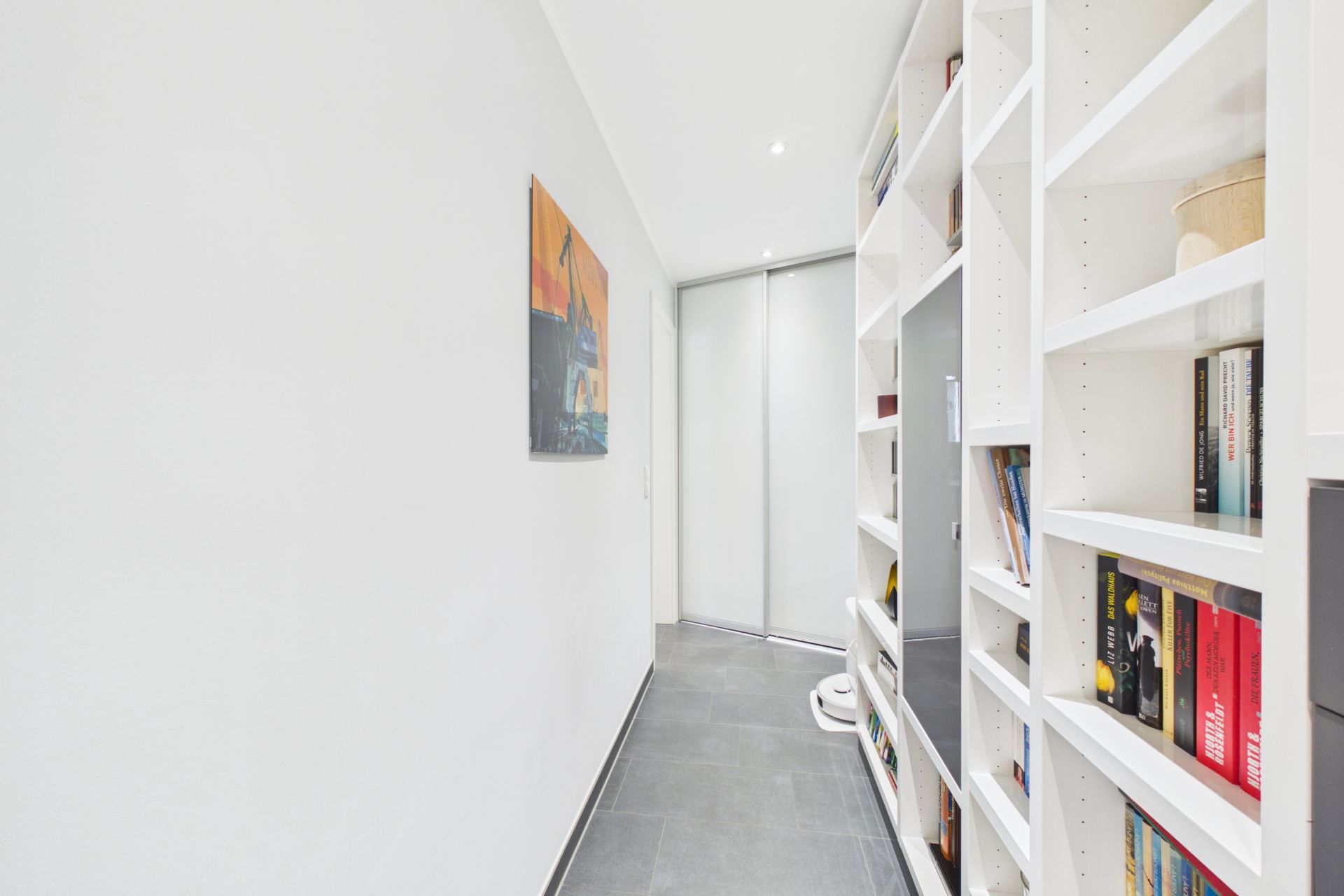 Heller Flur mit Bücherregal an der rechten Wand und einem Gemälde an der linken Wand.