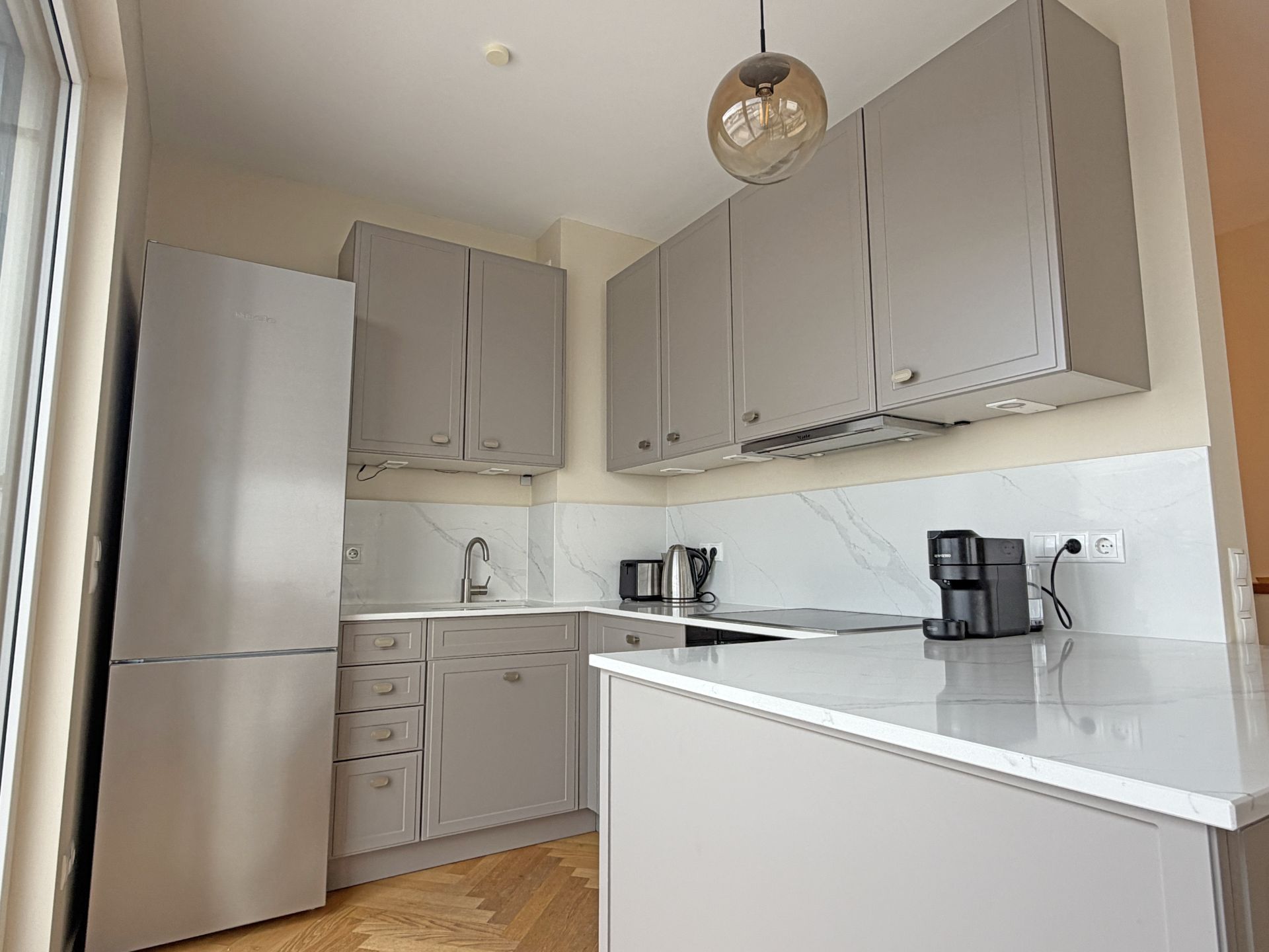 Moderne Küche mit grauen Schränken, Kühlschrank, Kaffeemaschine und Wasserkocher.