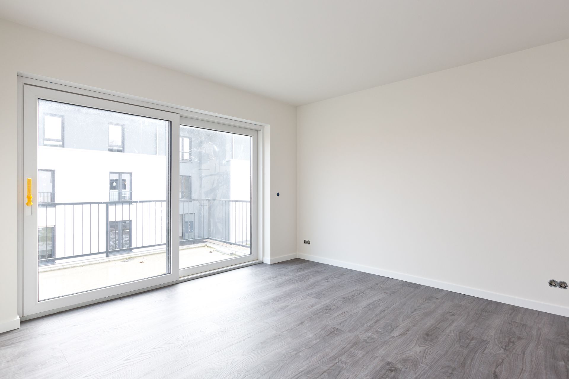 Leerer Raum mit grauem Boden und großer Glastür zu einem Balkon.