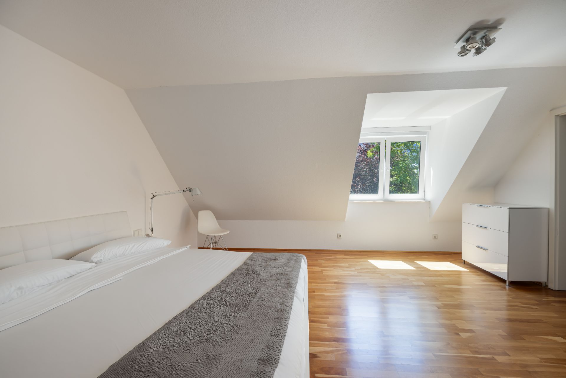 Helles Schlafzimmer mit Doppelbett, Holzfußboden, Fenster und weißer Kommode.
