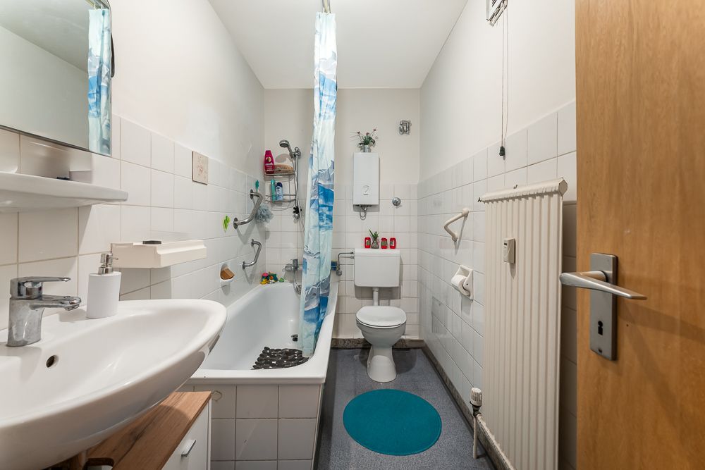 Kleines Badezimmer mit Badewanne, Waschbecken, Toilette und blauem Teppich.